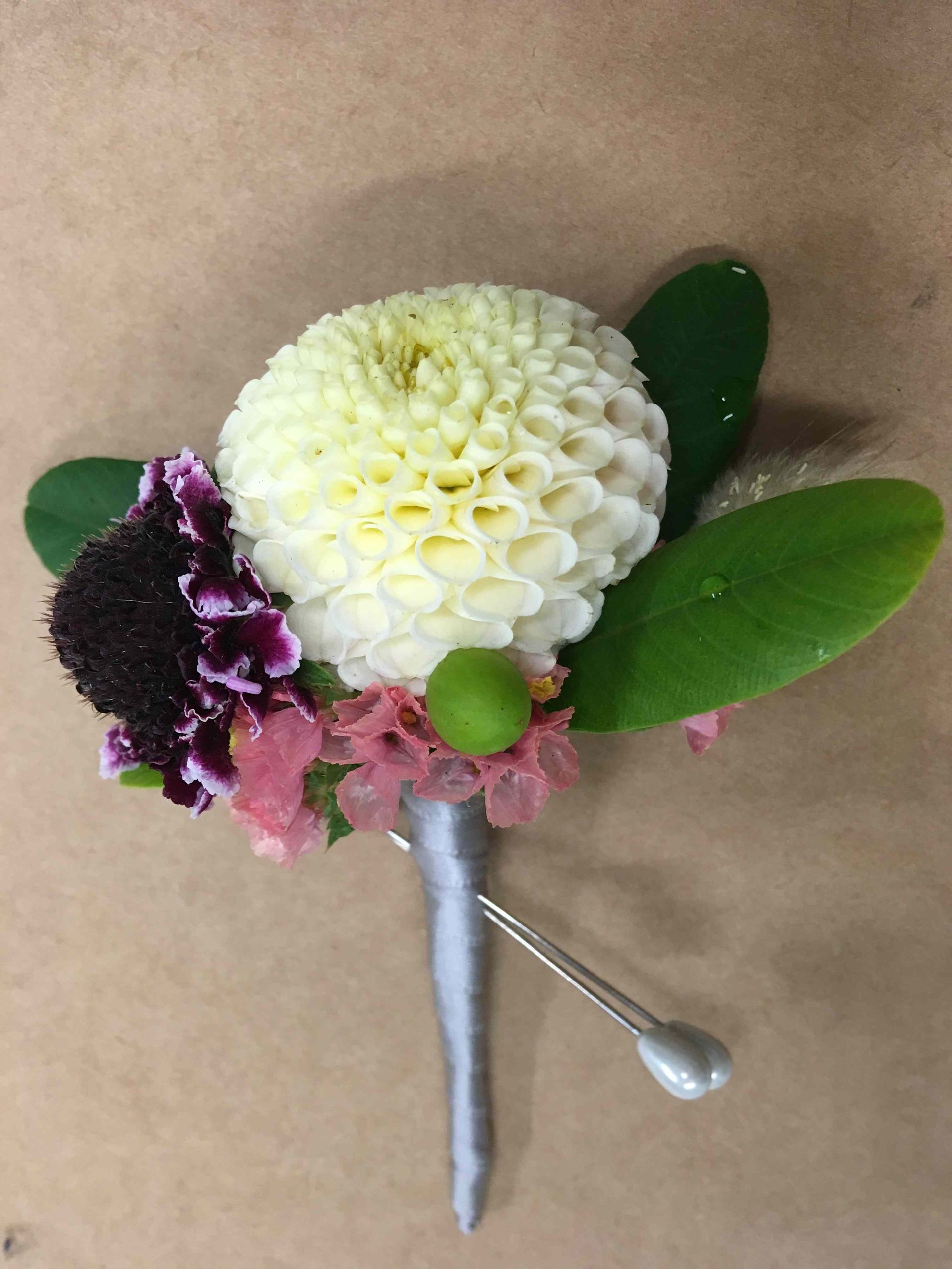A white flower with purple flowers and green leaves is on a pin.