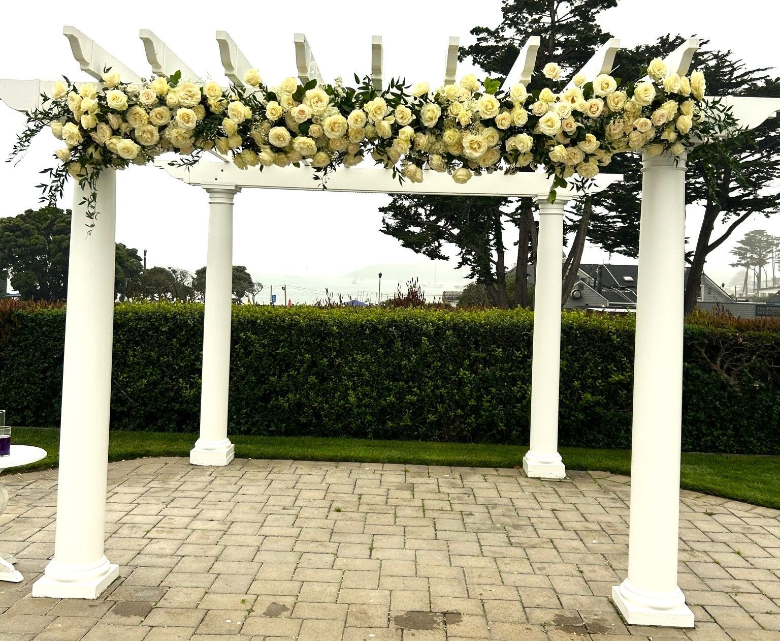 A white pergola decorated with white roses and greenery