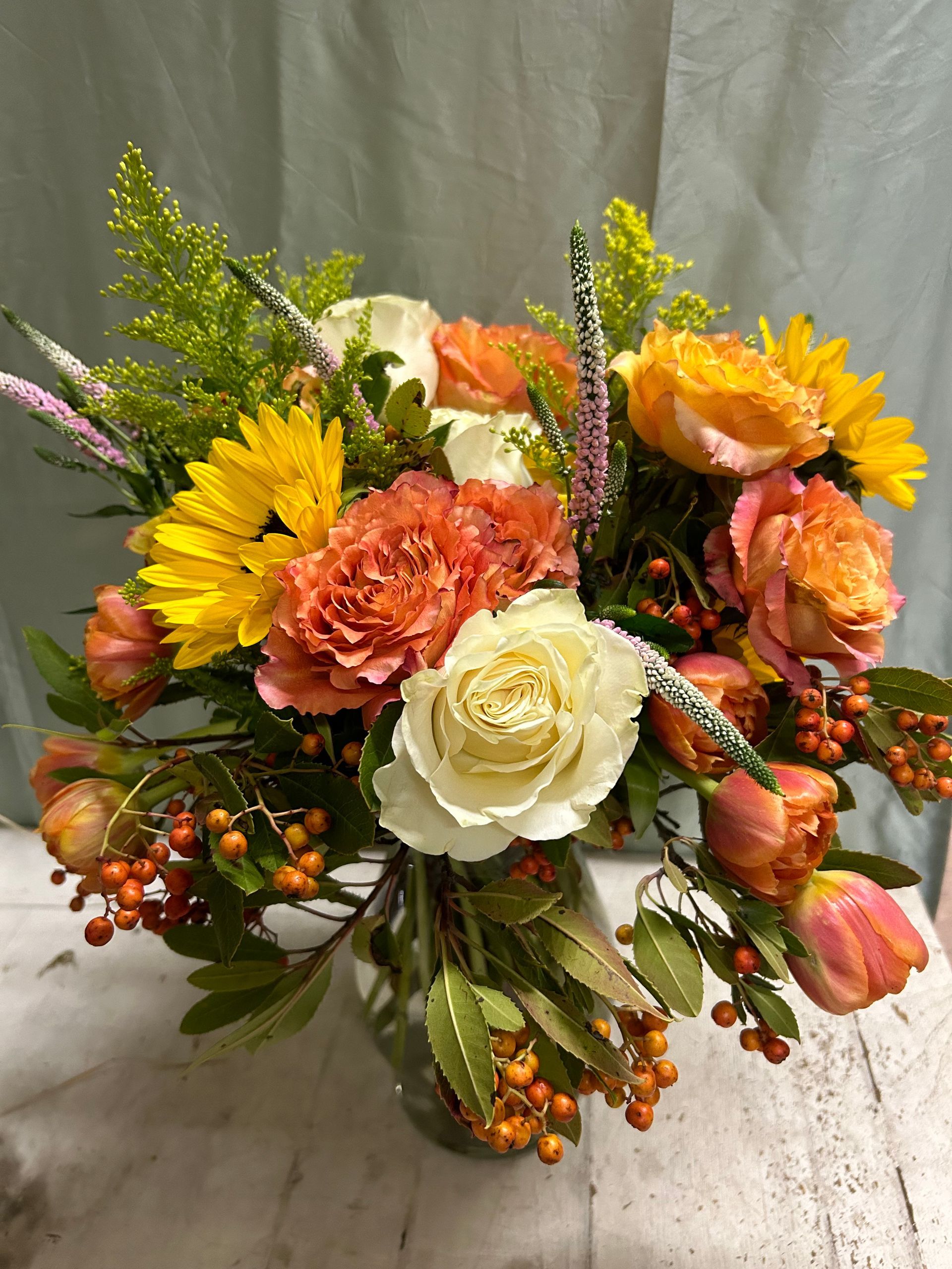 A vase filled with flowers and berries, sunflowers and veronicas