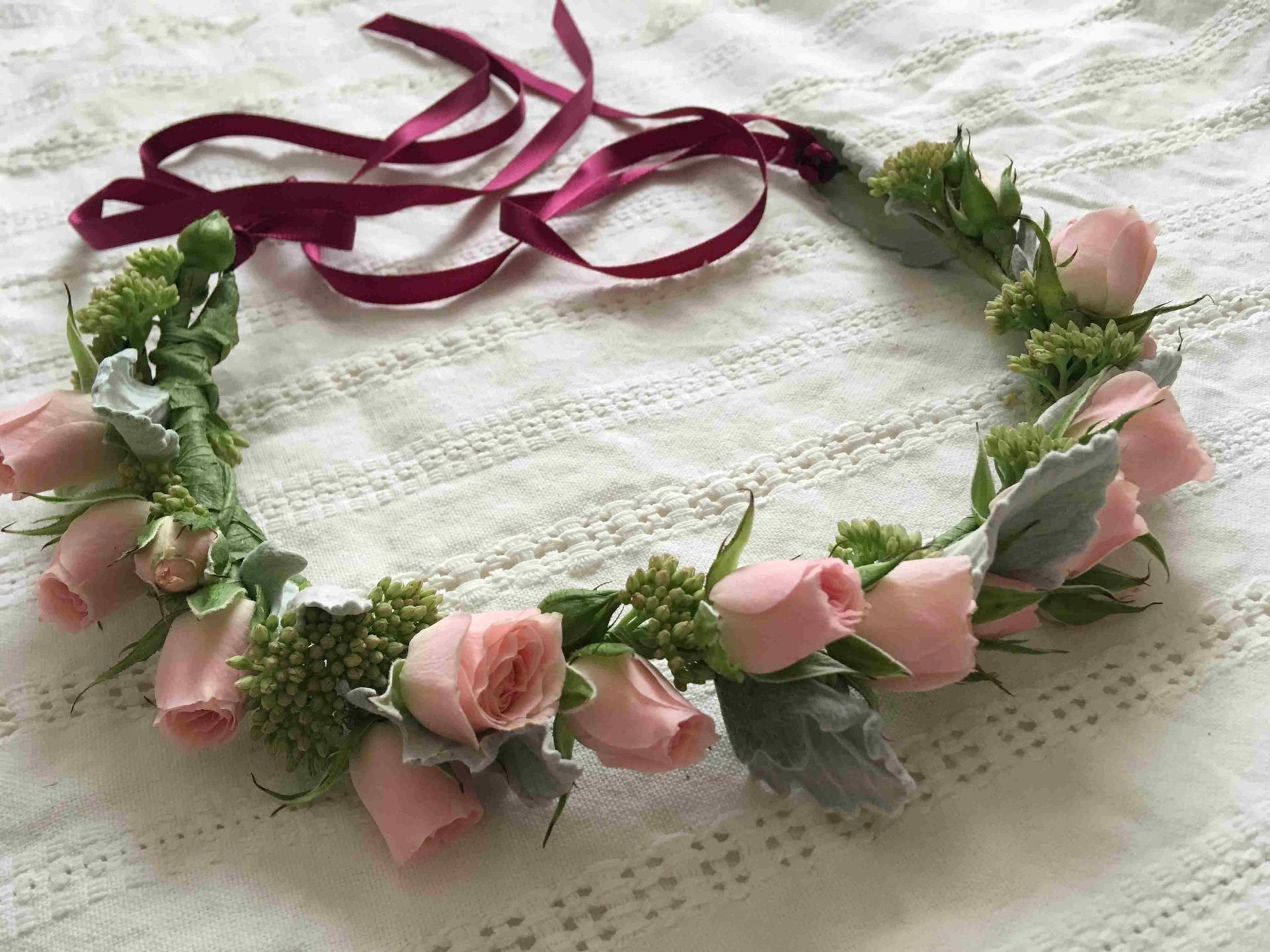 A flower crown with pink roses and greenery is sitting on a table.