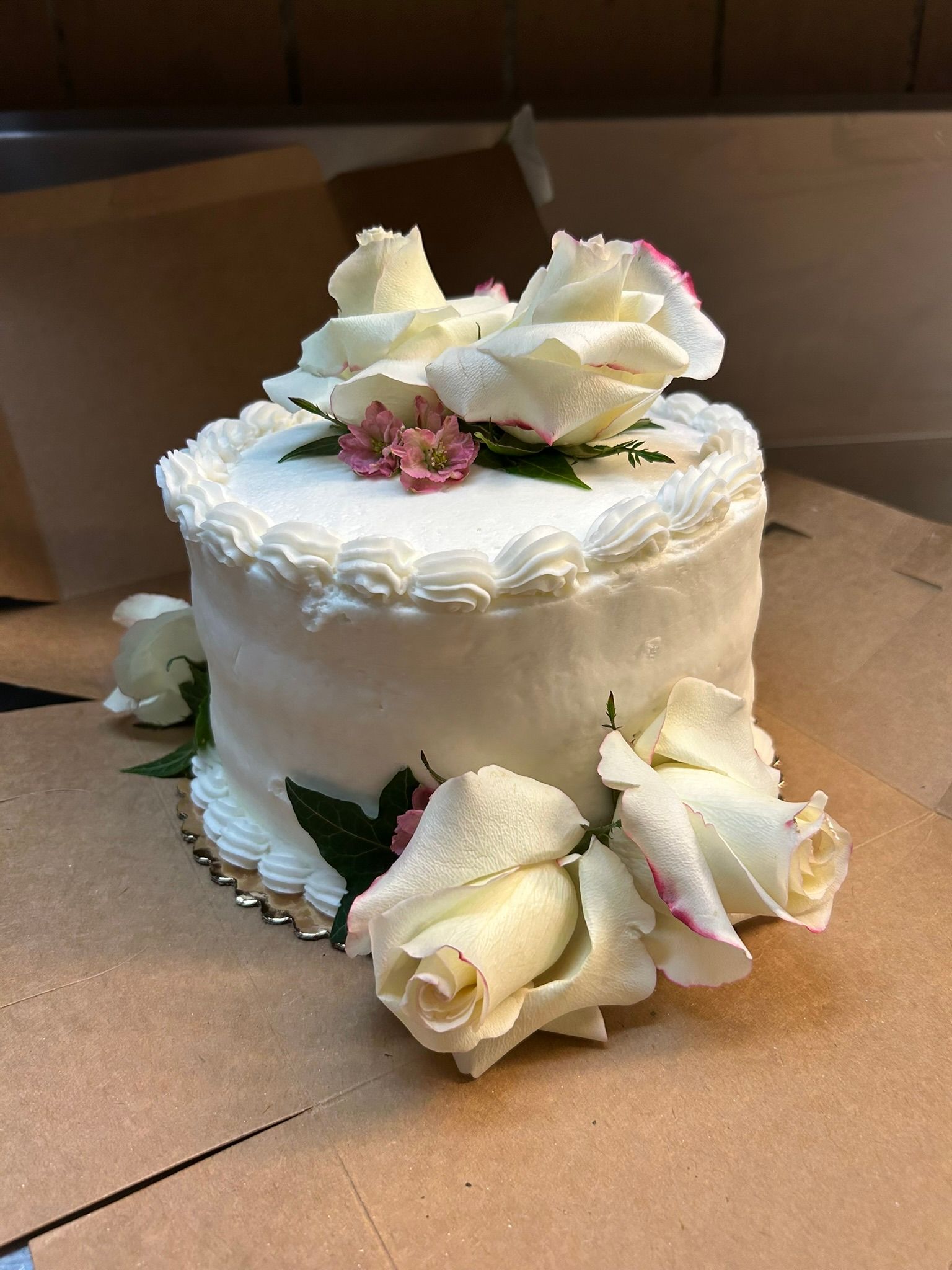 A white cake with roses on top of it is sitting on a table.