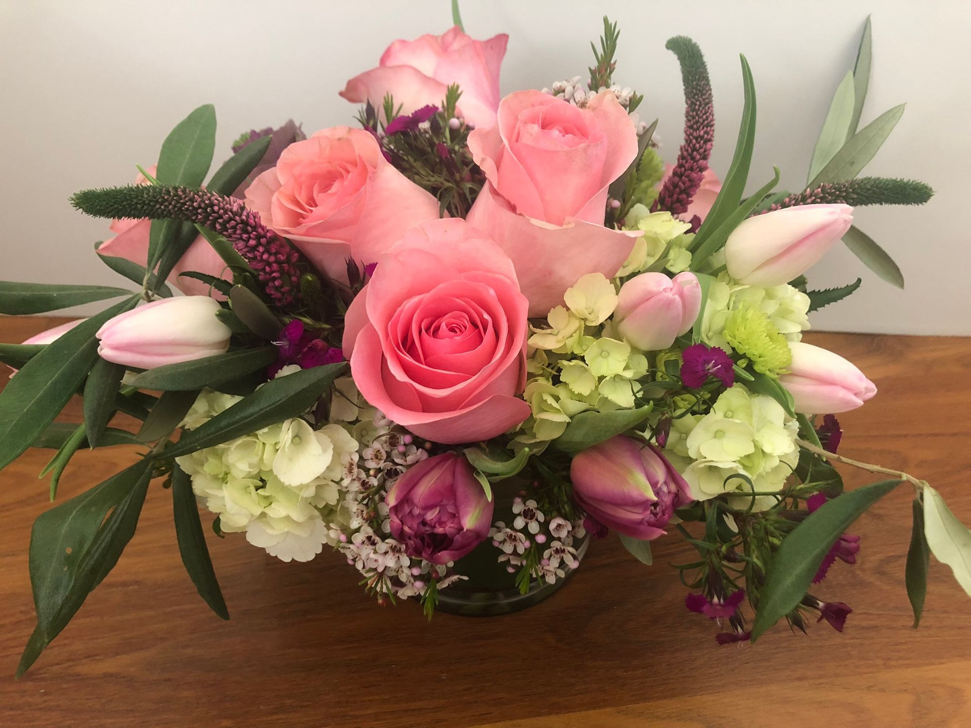 A vase filled with pink roses and other flowers on a wooden table.