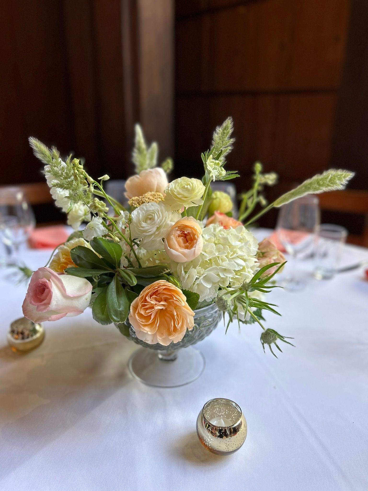 Floral centerpiece in a glass vase on a white tablecloth with pink and gold accents.