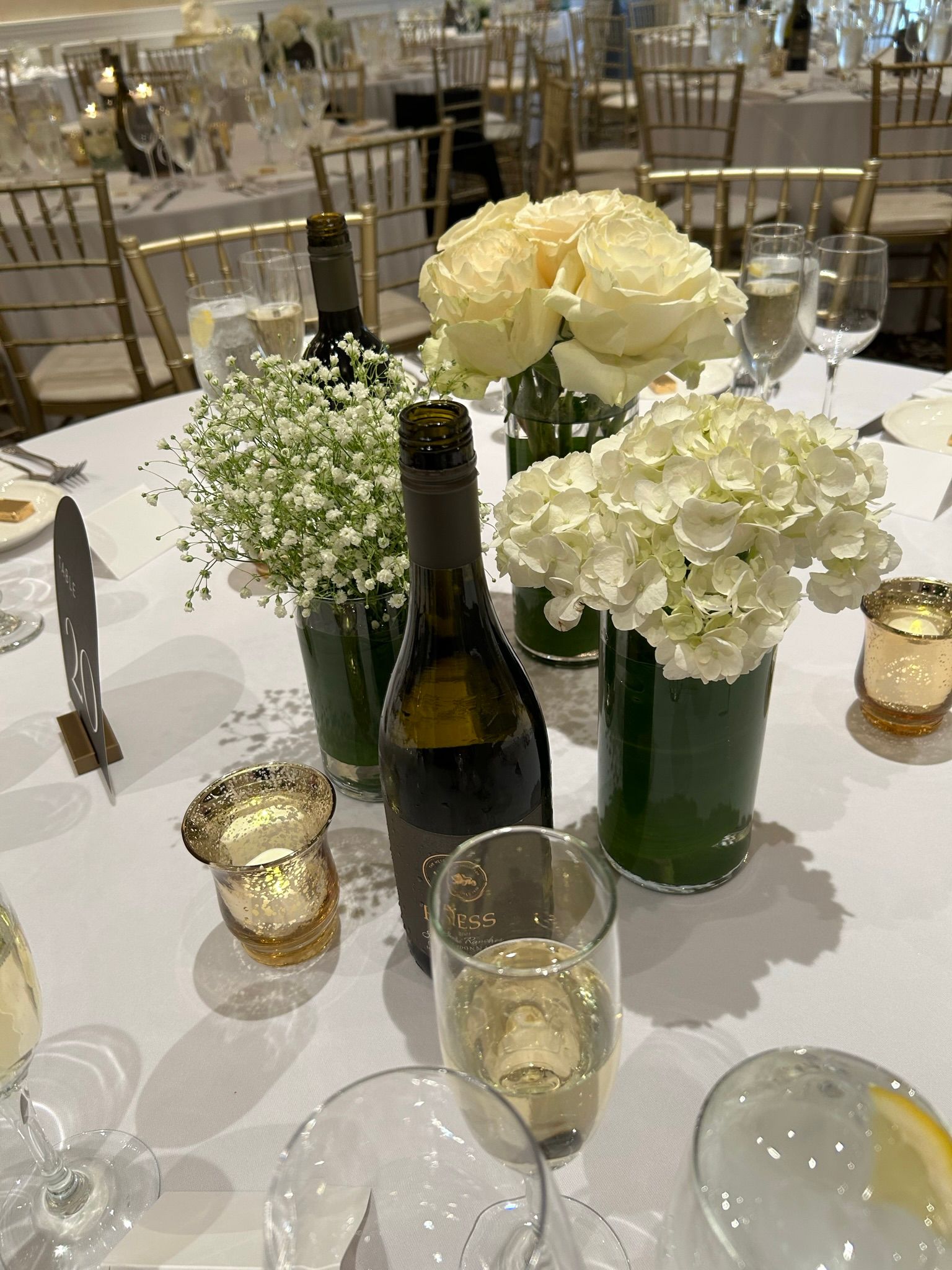 A table with a bottle of wine , vases of flowers , candles , and glasses of wine.