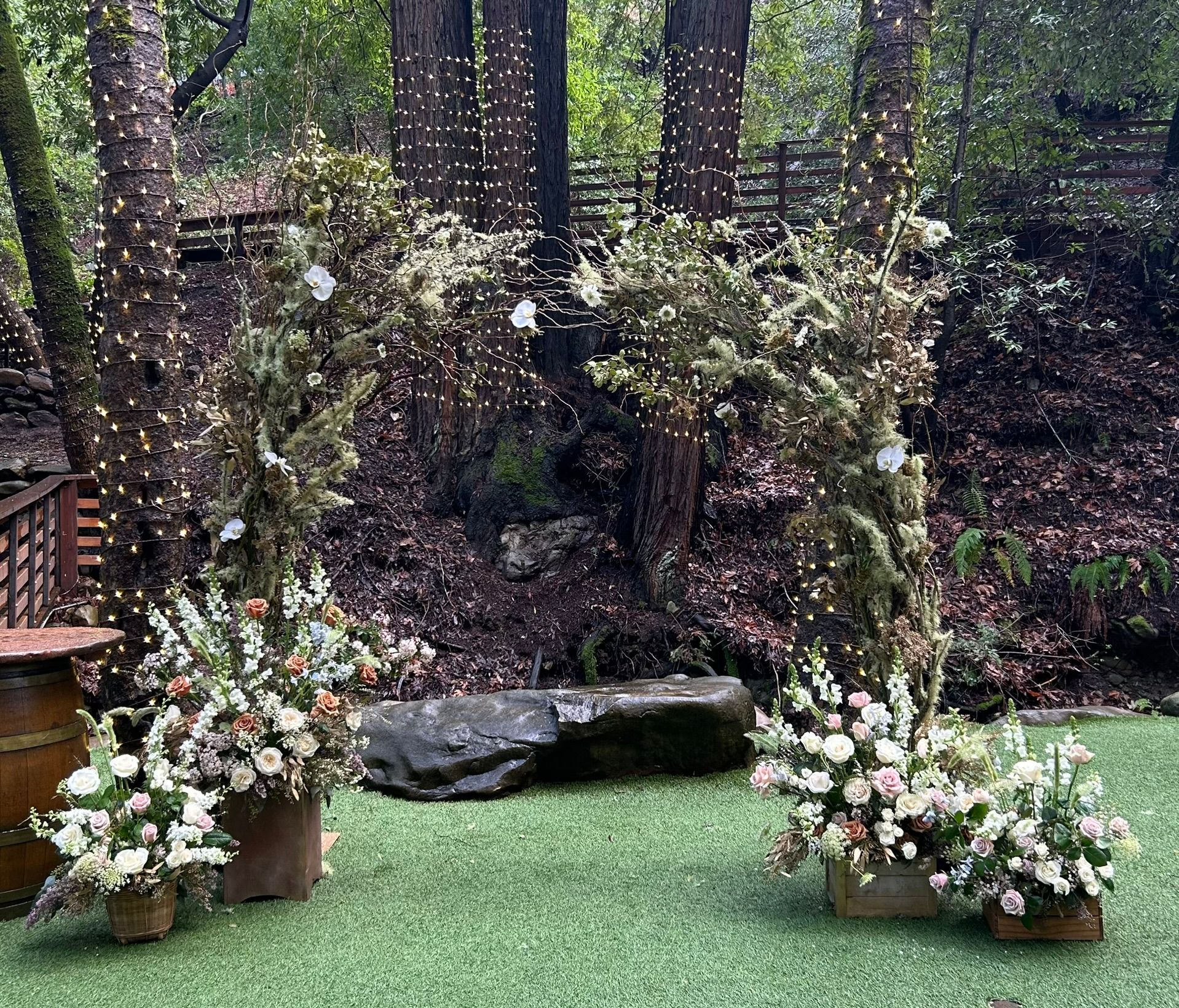 A wedding arch decorated with flowers and lights is sitting on top of a lush green field.