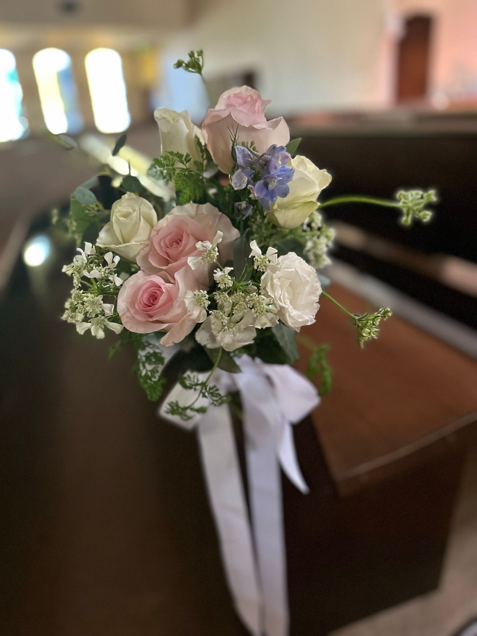 A bunch of flowers are sitting on a bench in a church.