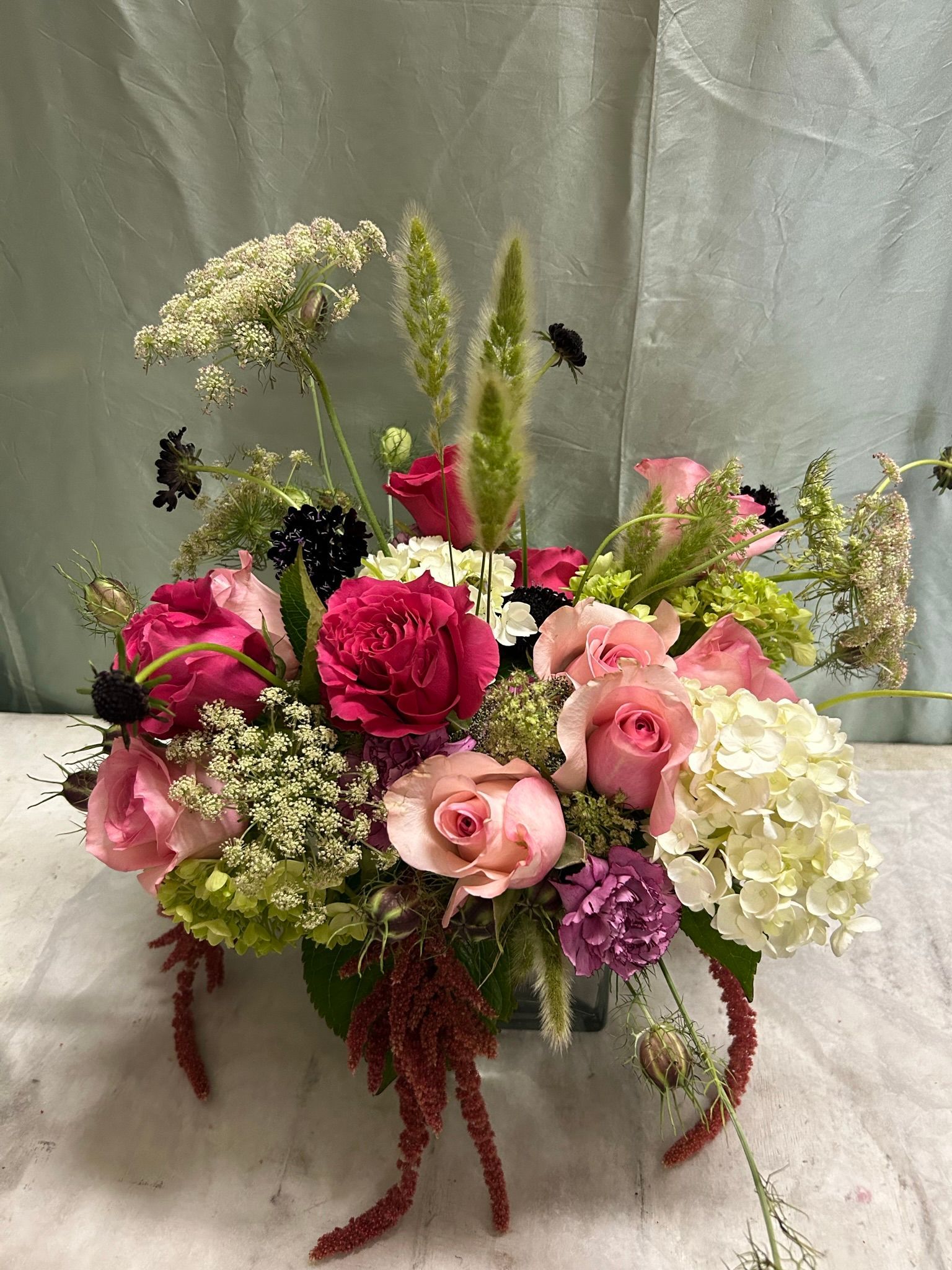 A vase filled with pink and purple flowers, grasses and Queen Anne's lace