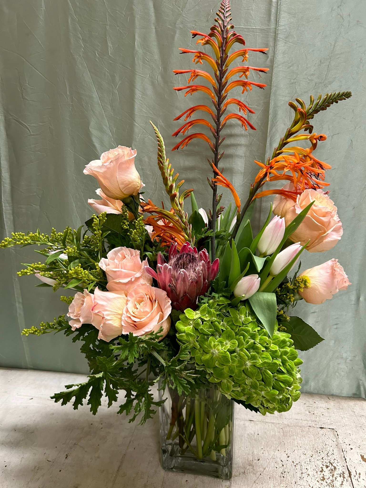 A vase filled with flowers and greenery is sitting on a table.