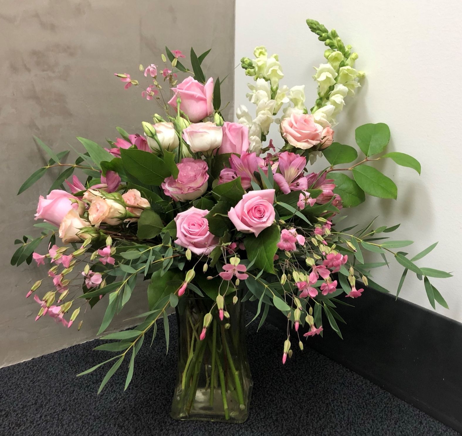 A vase filled with pink and white flowers is sitting on the floor.