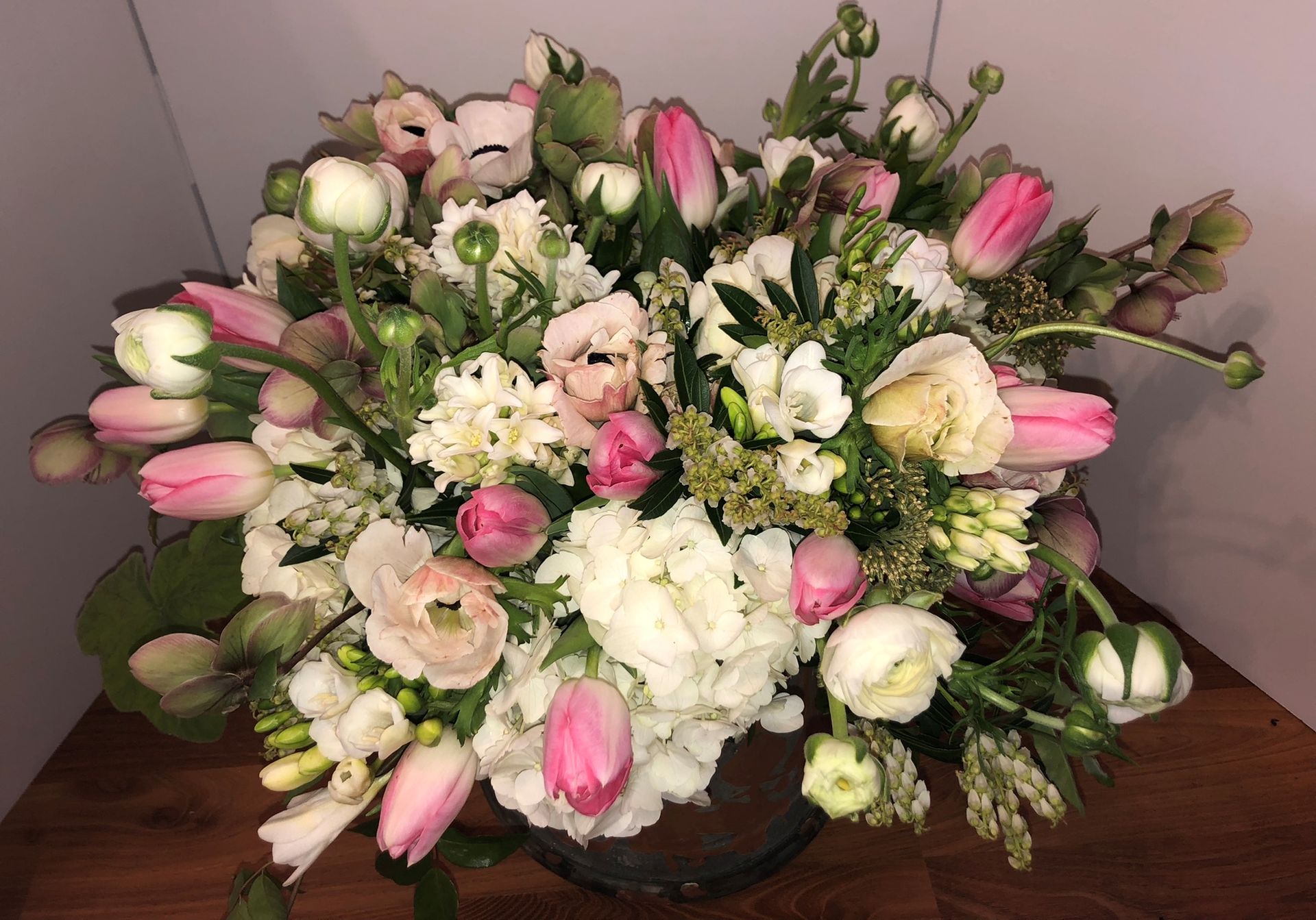 A vase filled with pink and white flowers is sitting on a wooden table.