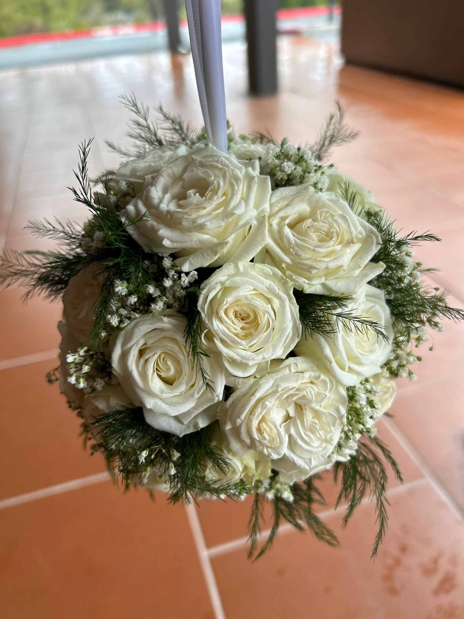 A bouquet of white roses hanging from a pole on a tiled floor.