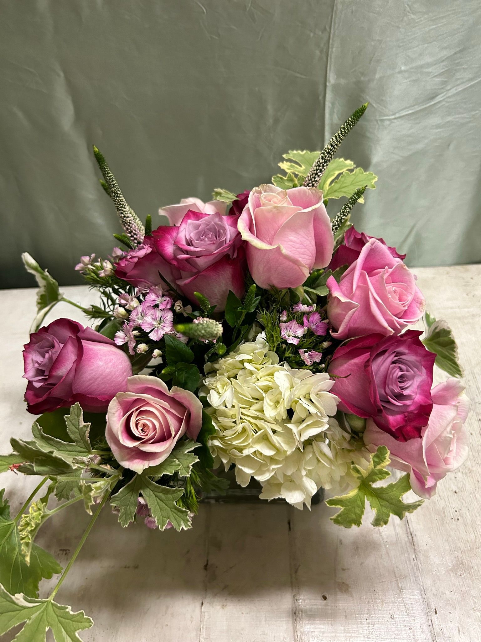 A vase filled with pink roses and greenery is sitting on a table.