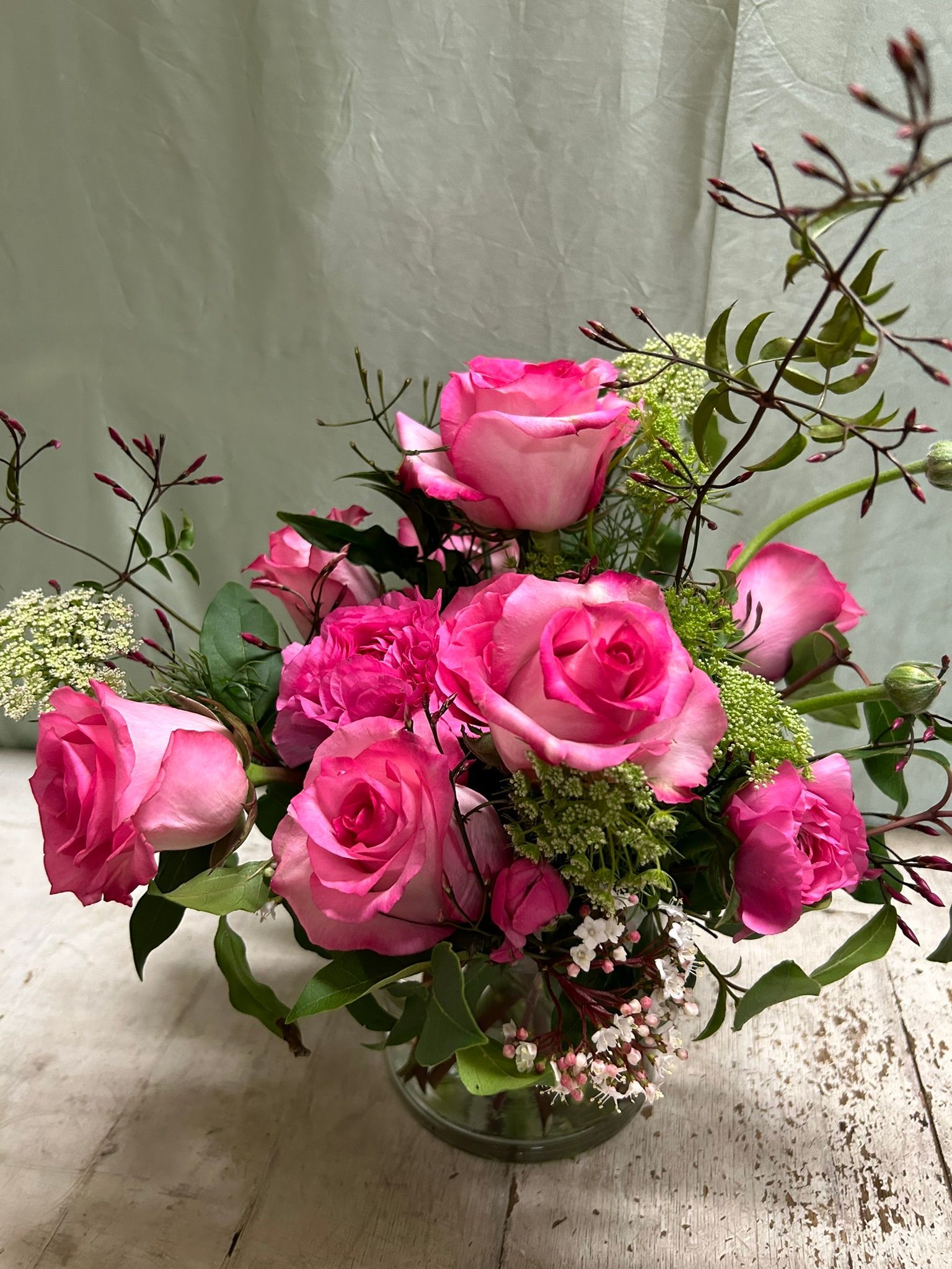 A vase filled with pink roses and greenery 