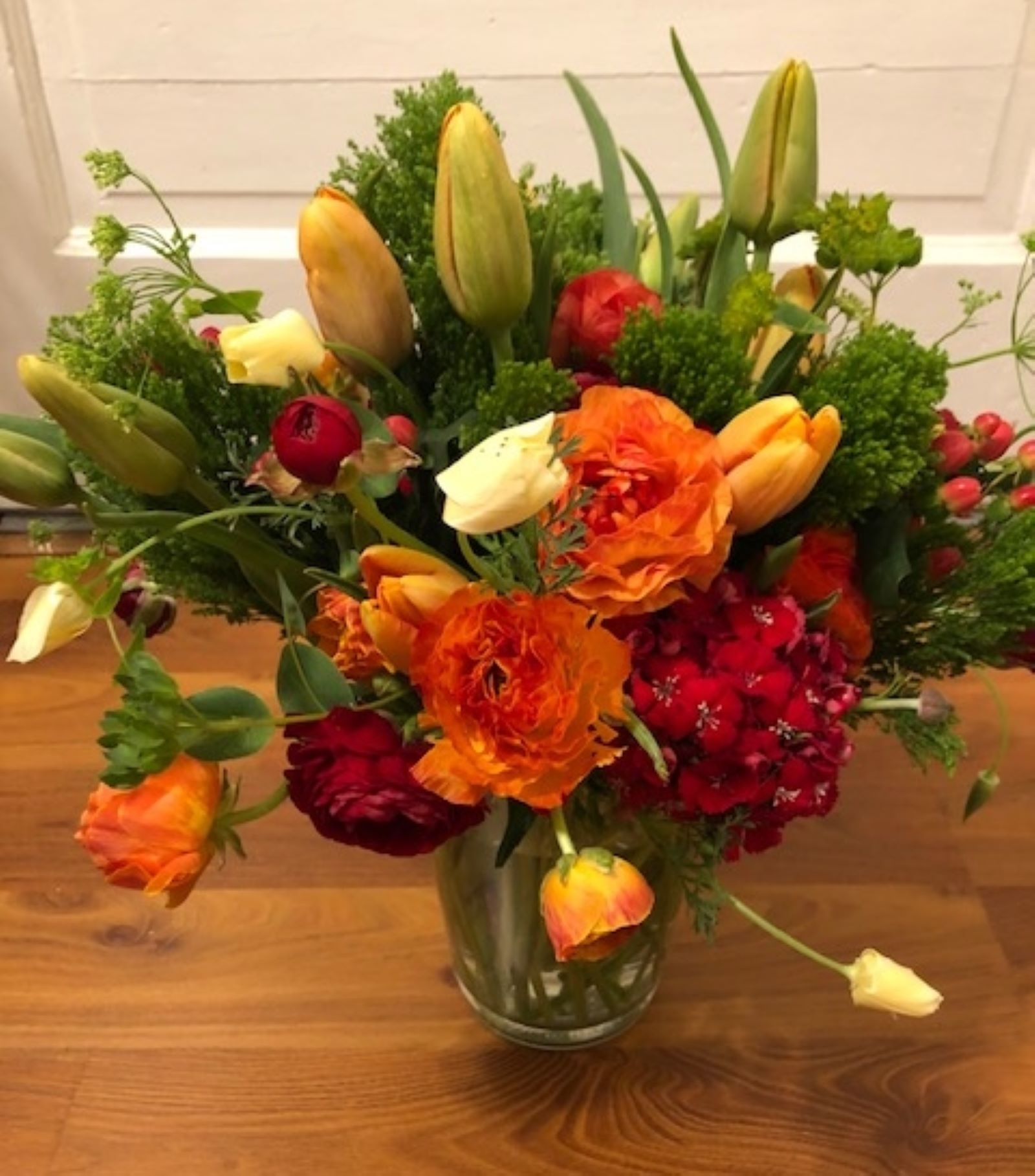 A vase filled with orange and red flowers sits on a wooden table