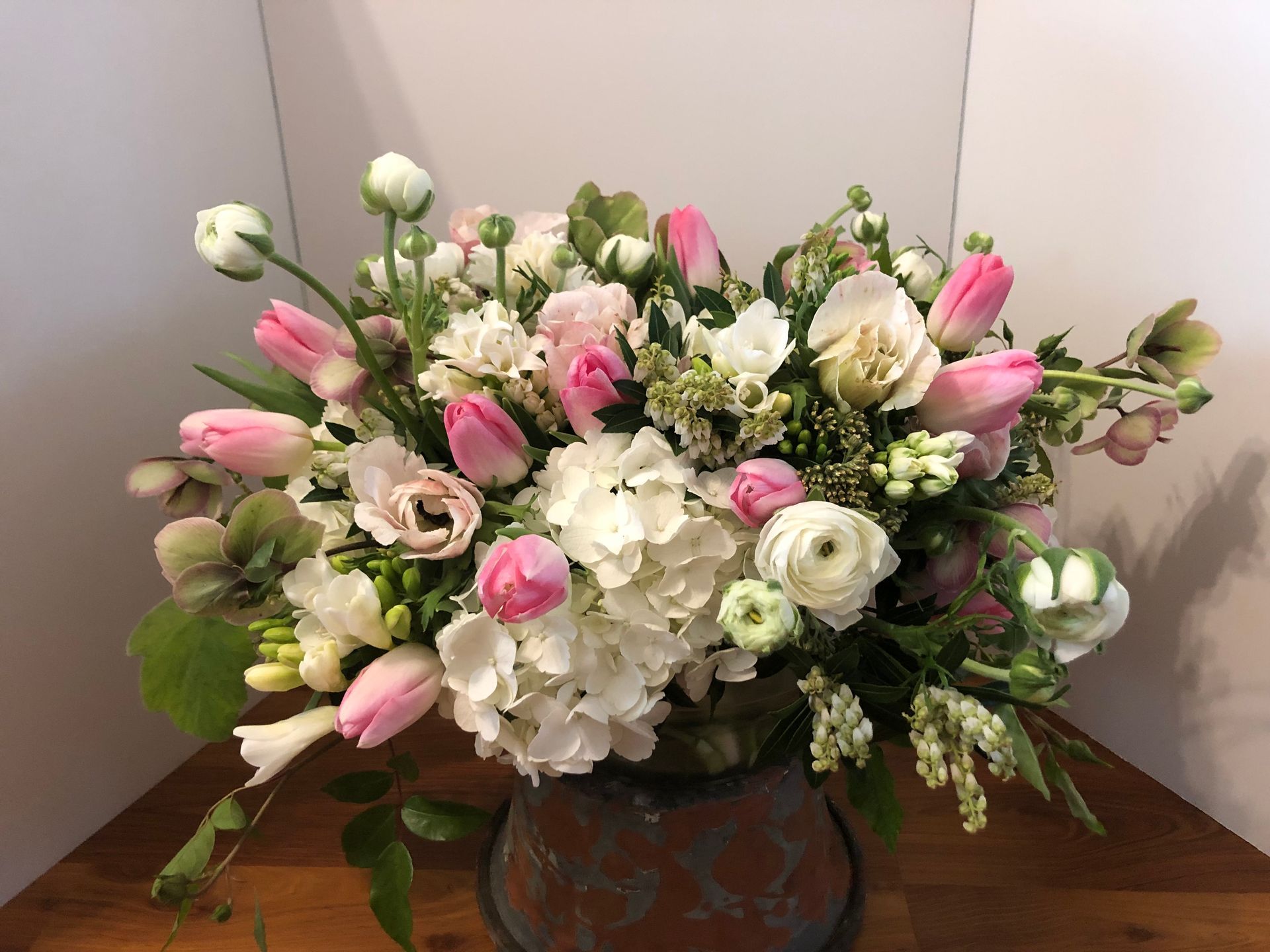 A vase filled with pink and white flowers is sitting on a wooden table.
