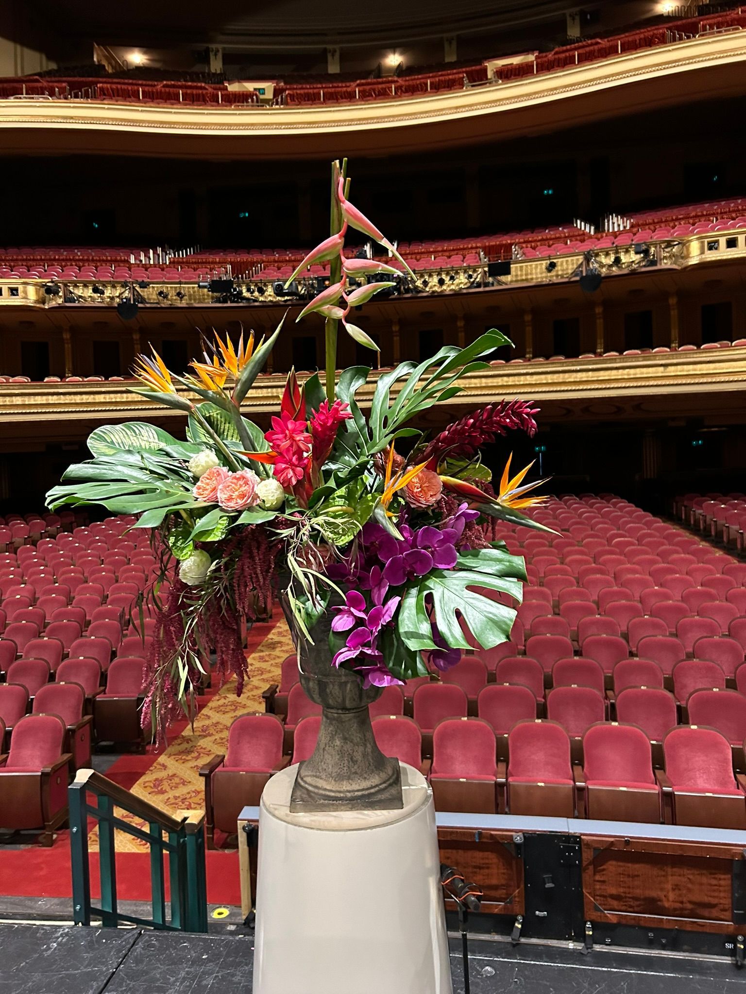 A vase filled with flowers is sitting on a stage in front of an empty auditorium.