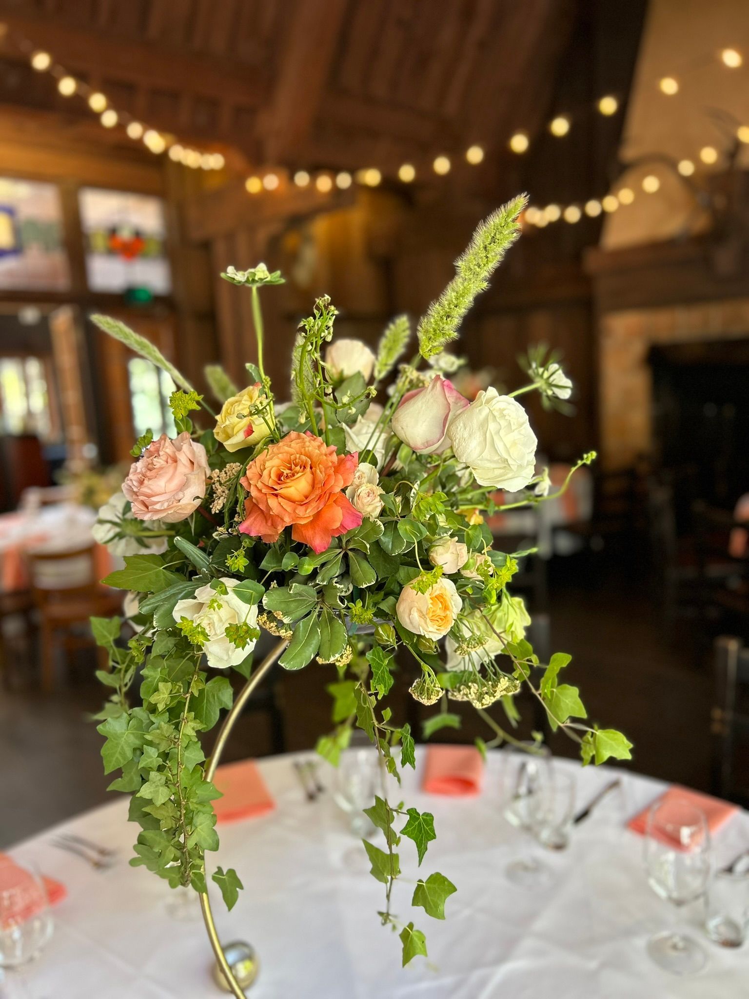 Floral centerpiece on a table set for a celebration, with orange, pink, and white blooms; ivy cascades.