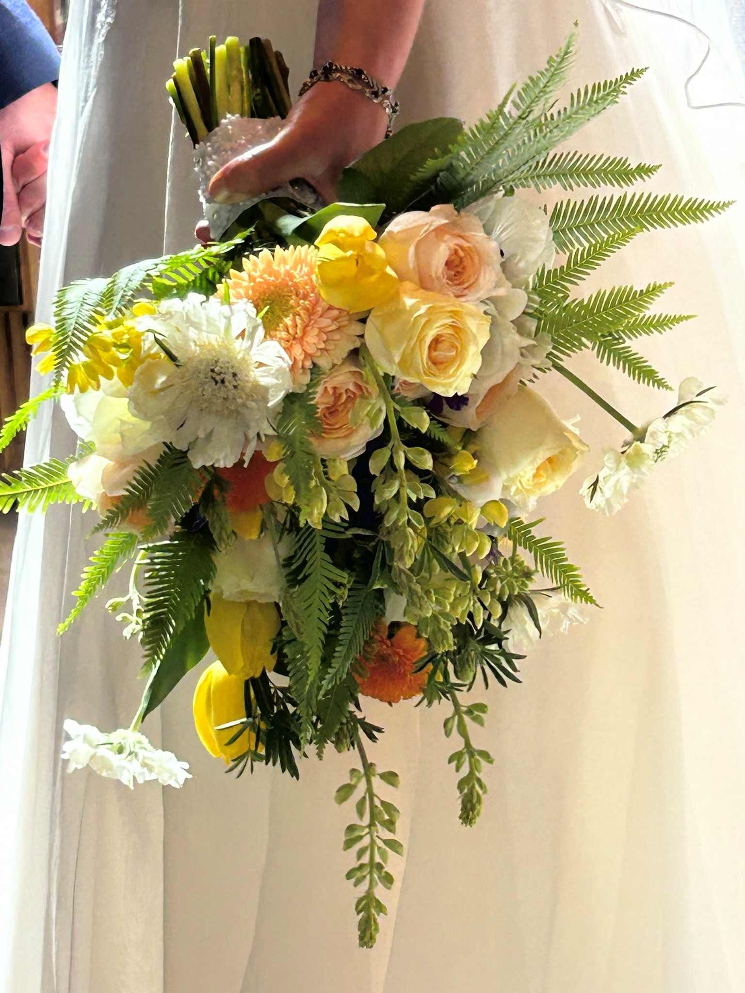 A bride is holding a spring bouquet of yellow and white flowers.
