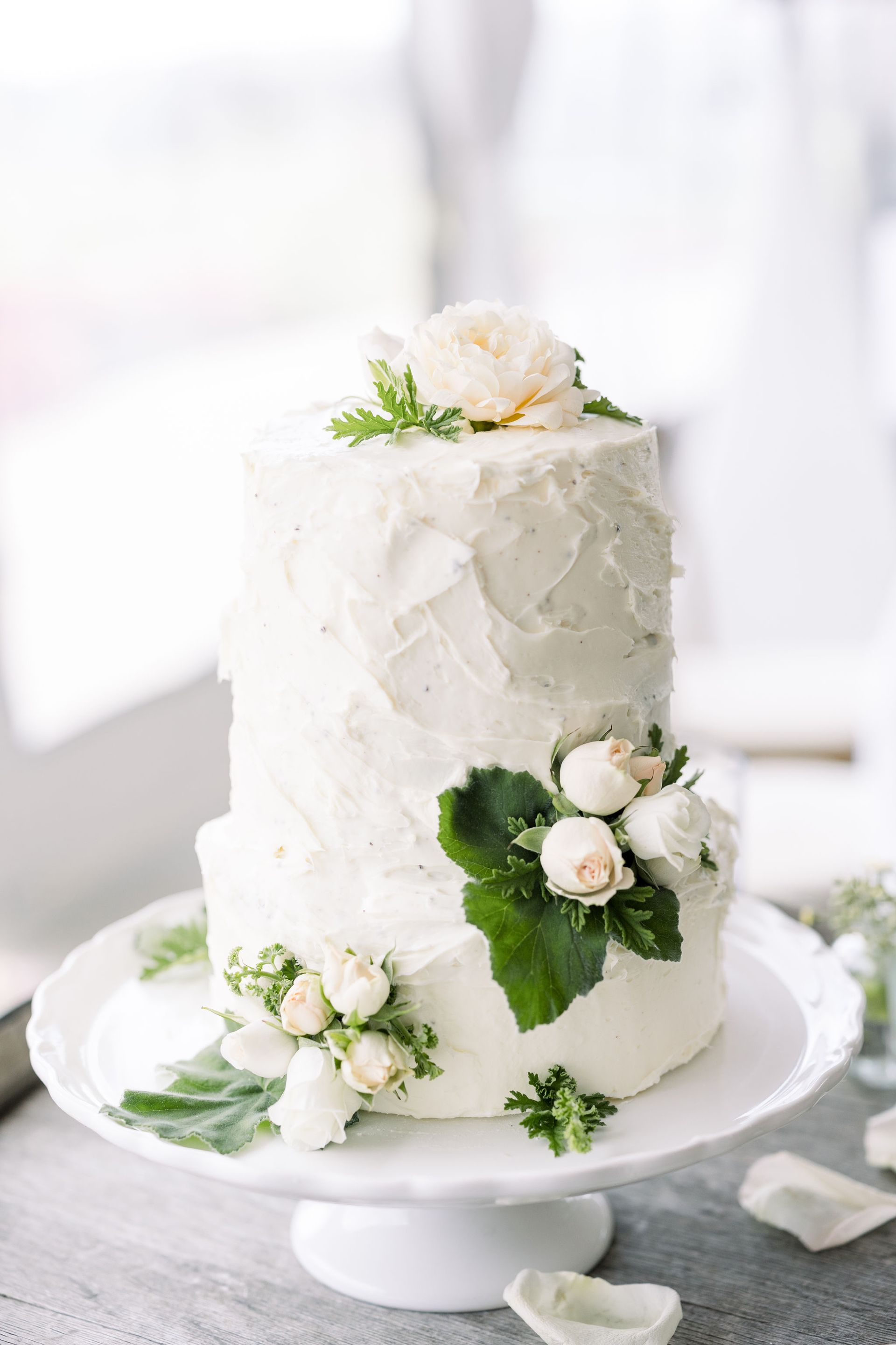 Two-tiered white wedding cake with floral accents, set on a white cake stand.