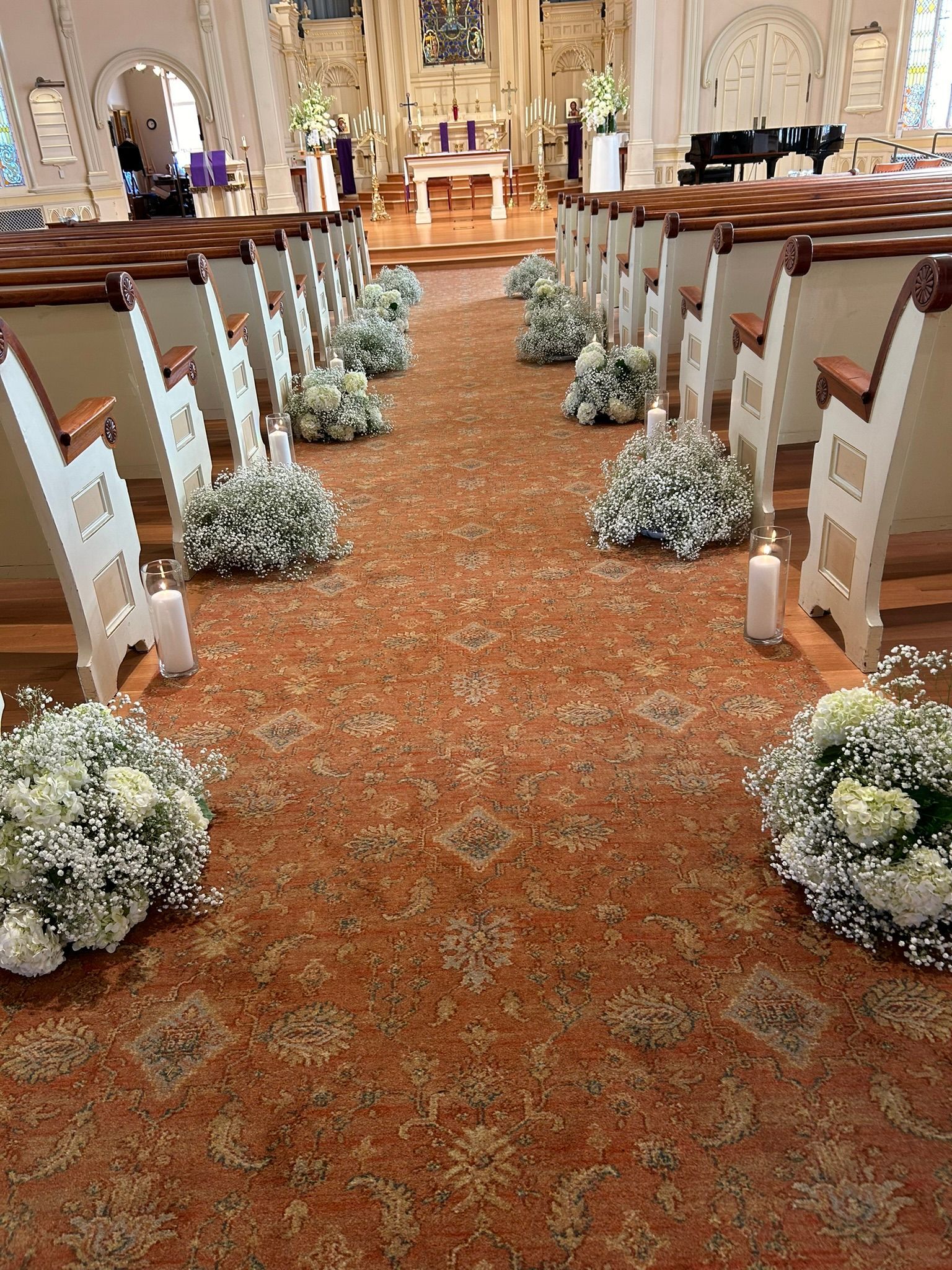 A church aisle decorated with baby 's breath designs and candles for a wedding ceremony.
