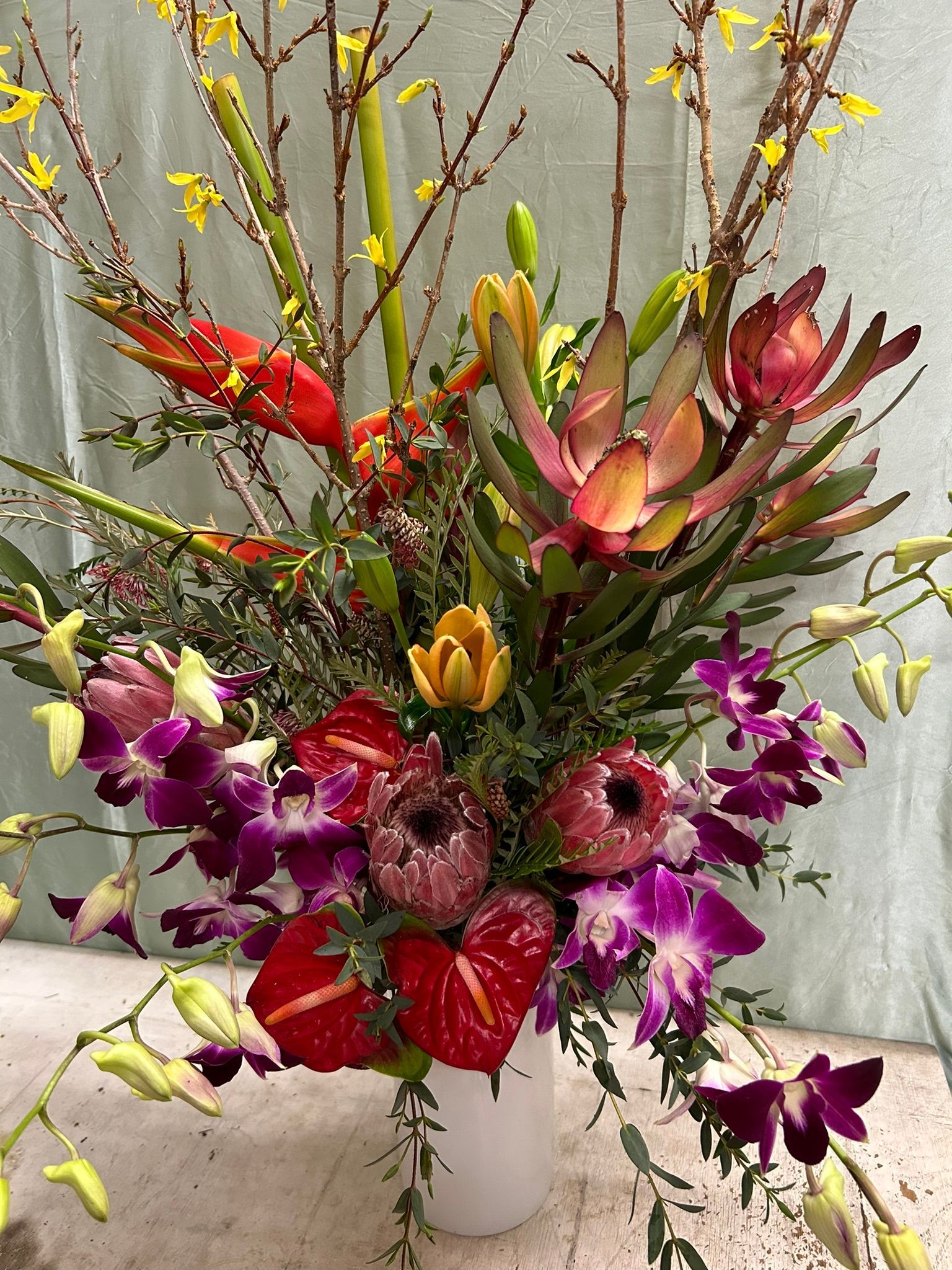 A vase filled with a tropical flowers, heliconia, forsythia and lilies