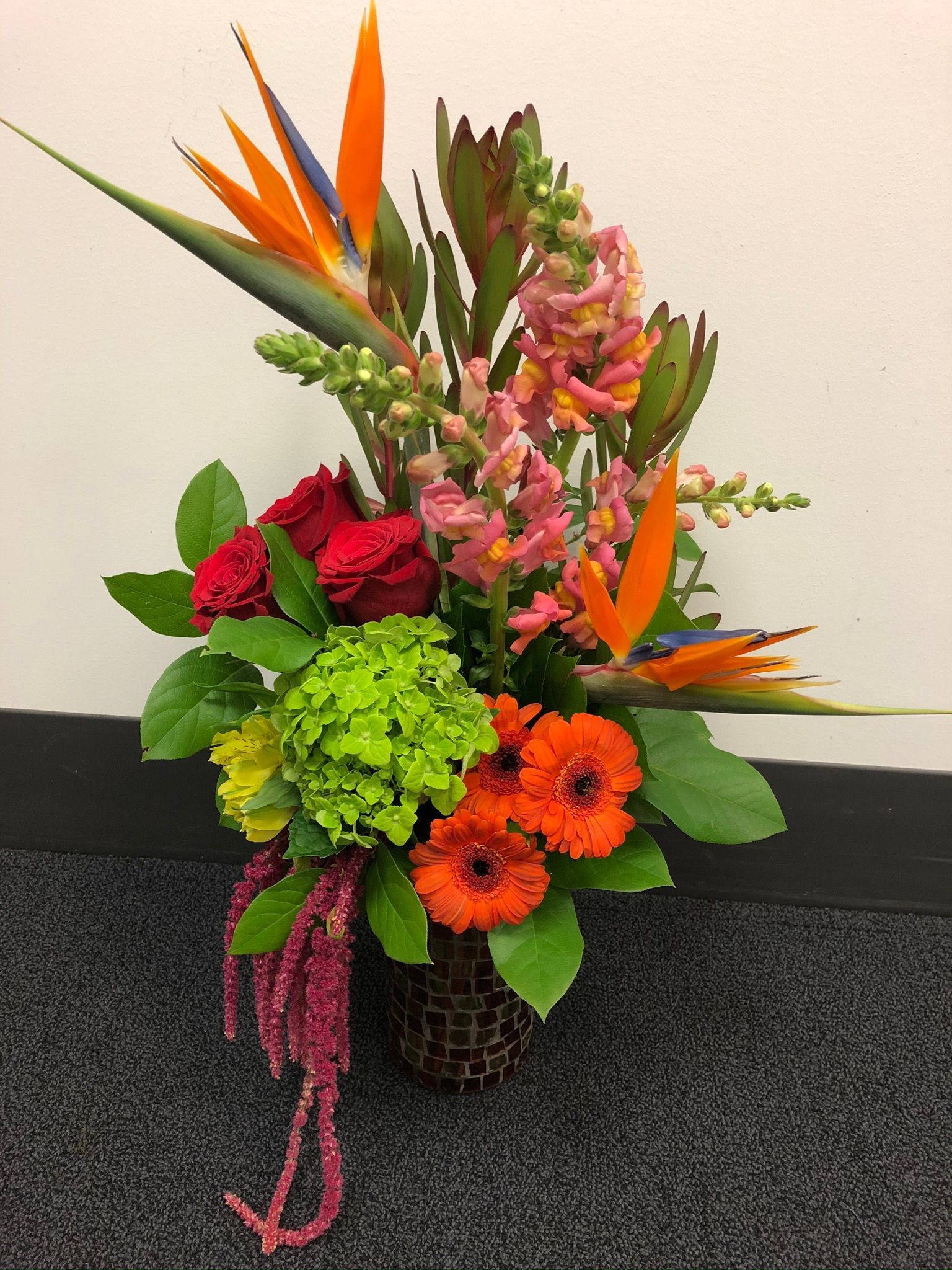 A vase filled with bright colors flowers such as bird of paradise and snapdragons