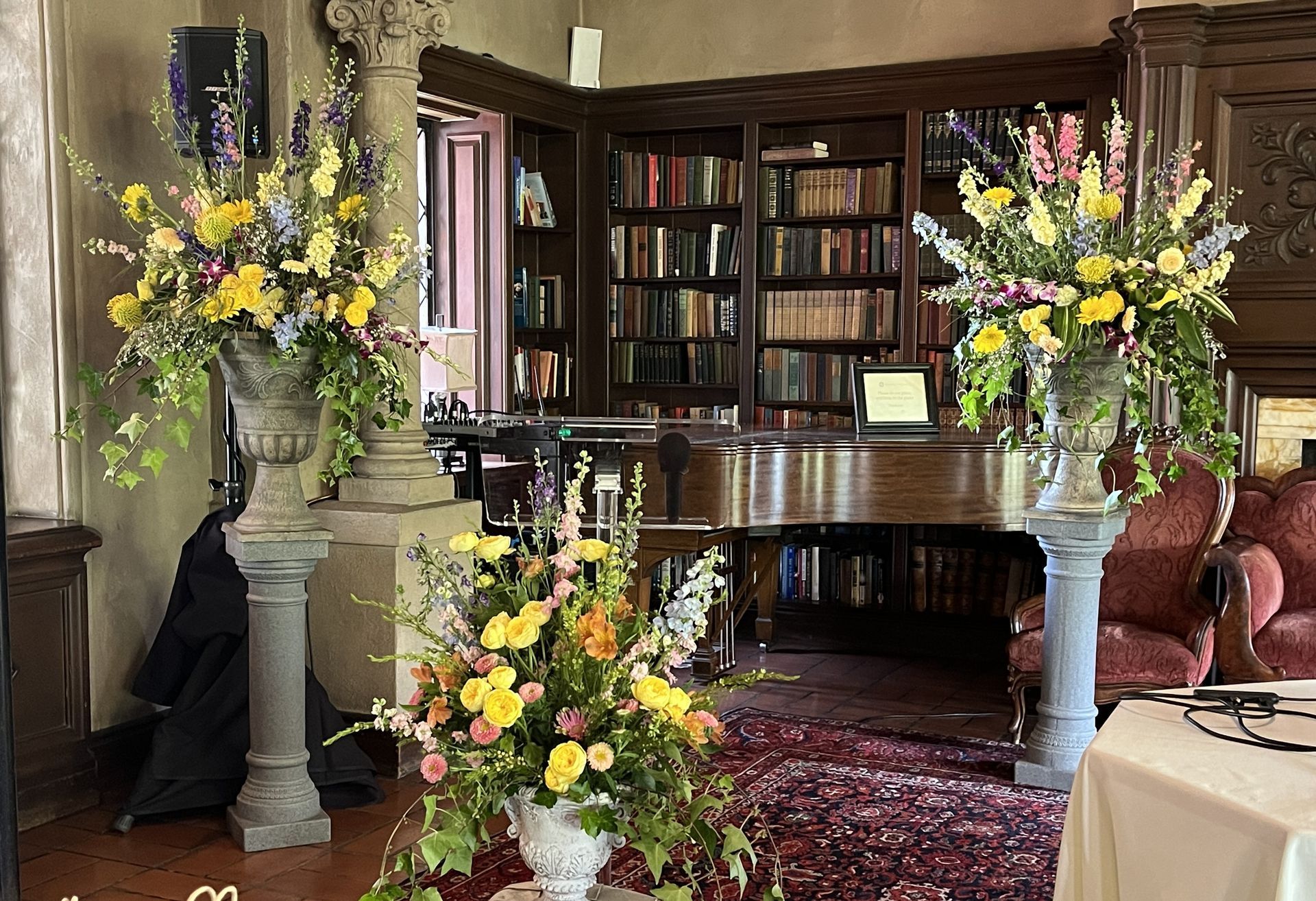 Ornate library interior with flower arrangements, a grand piano, and bookshelves.
