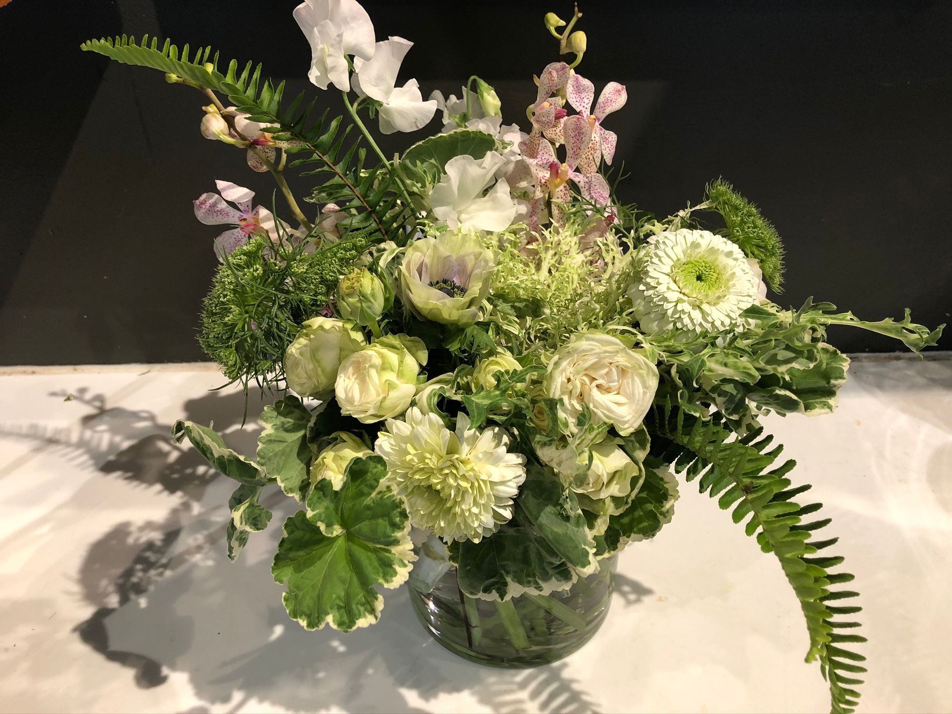 A vase filled with flowers and ferns is sitting on a table.