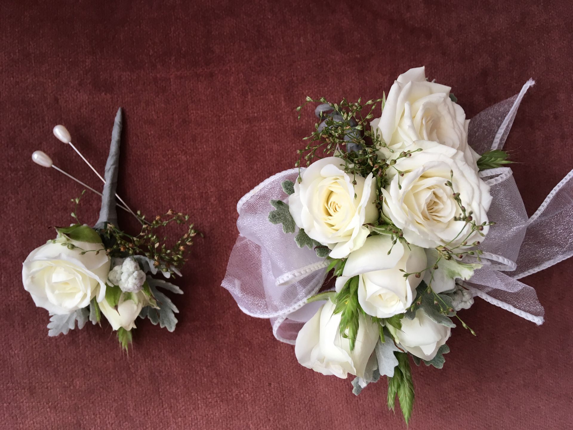A bouquet of white roses and a boutonniere are on a table.