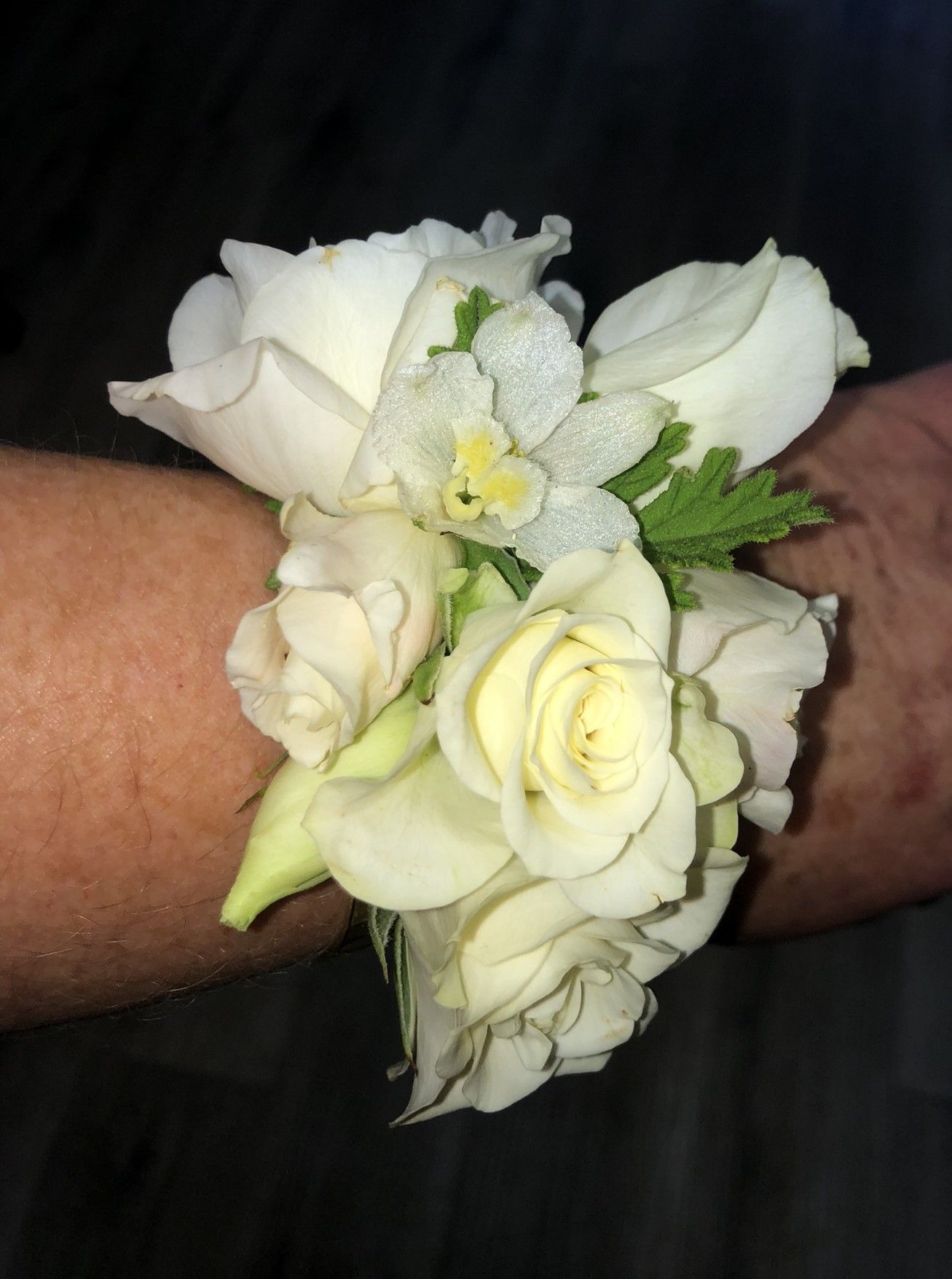 A person is wearing a wrist bouquet of white flowers.