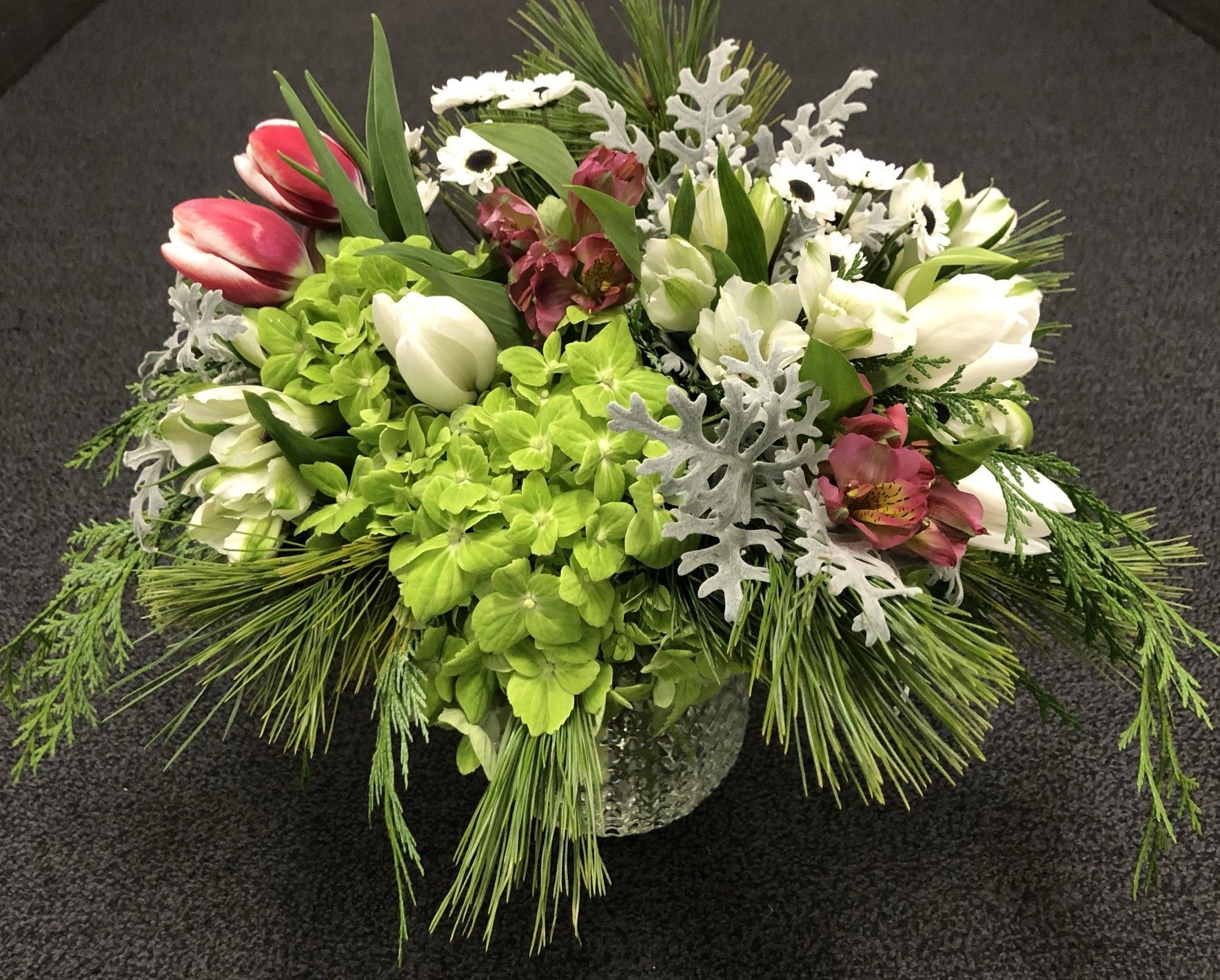 A Christmas winter vase filled with tulips, hydrangeas and greenery 