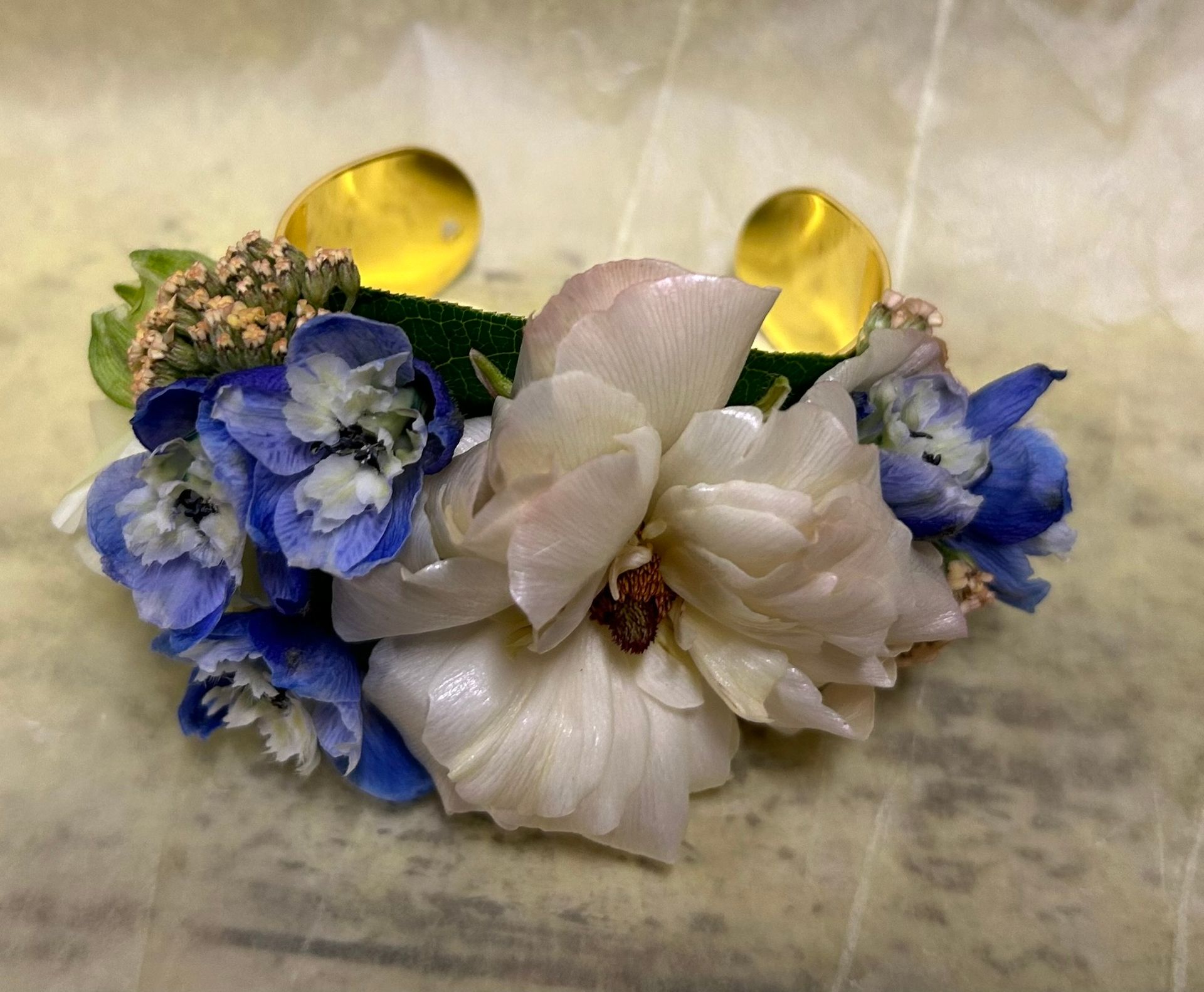 Floral wrist corsage with blue and white flowers, gold accents.