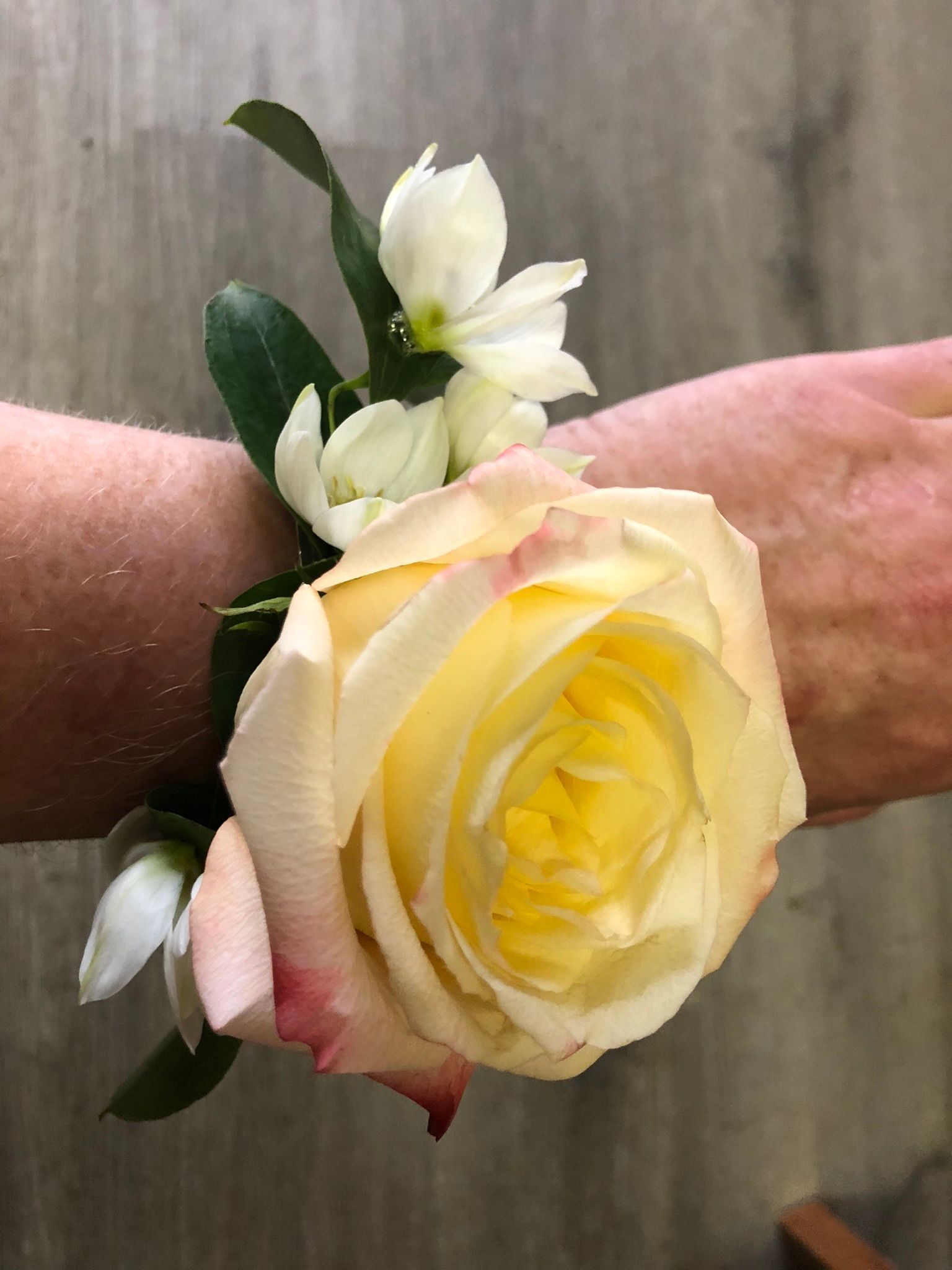 A person is wearing a wristband with a yellow rose and white flowers.