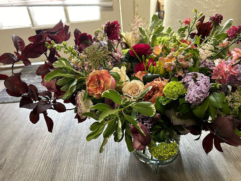 A bouquet of red, orange, yellow, and purple flowers in a clear vase on a table