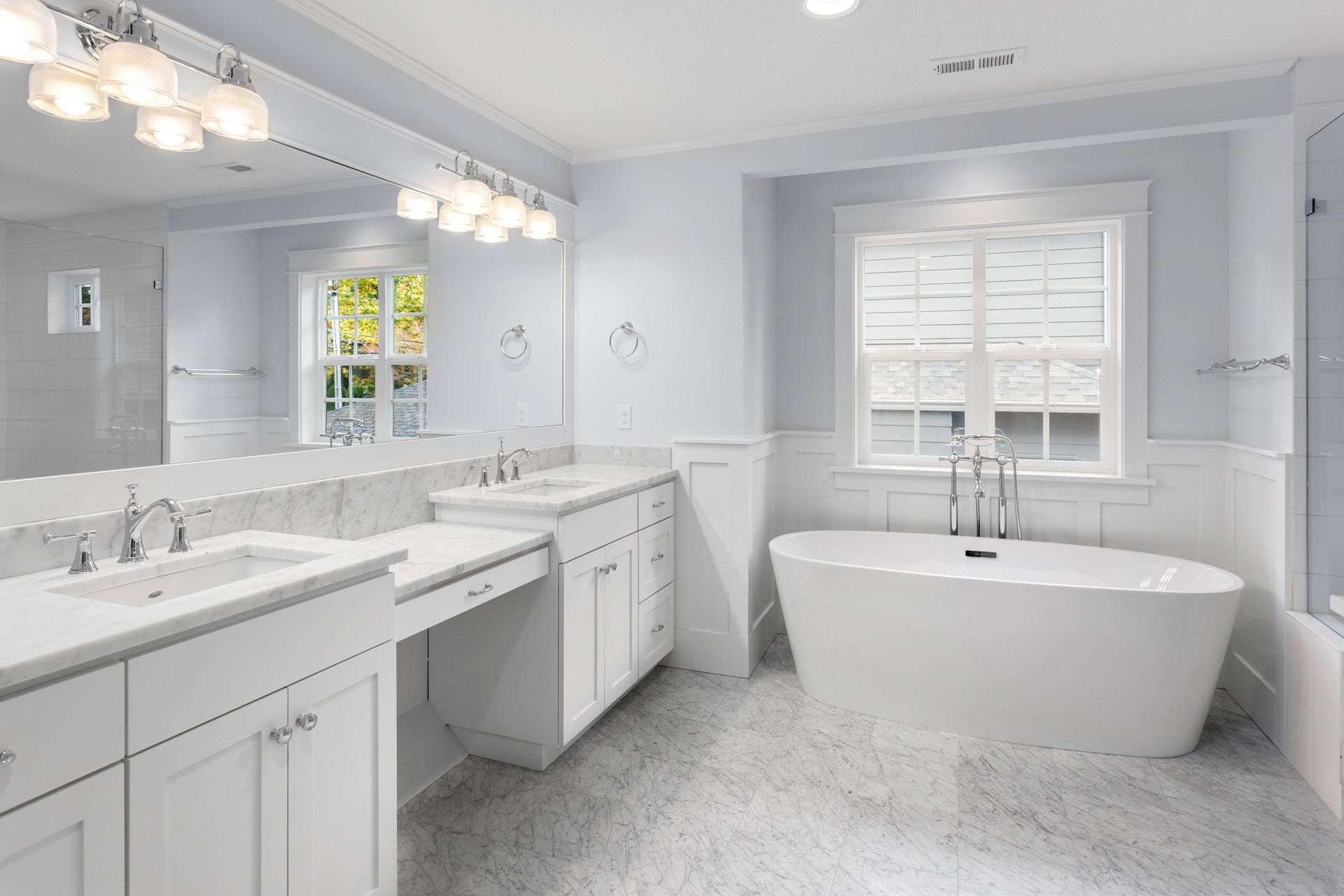 Bright white bathroom with a freestanding tub, double vanity, and window.