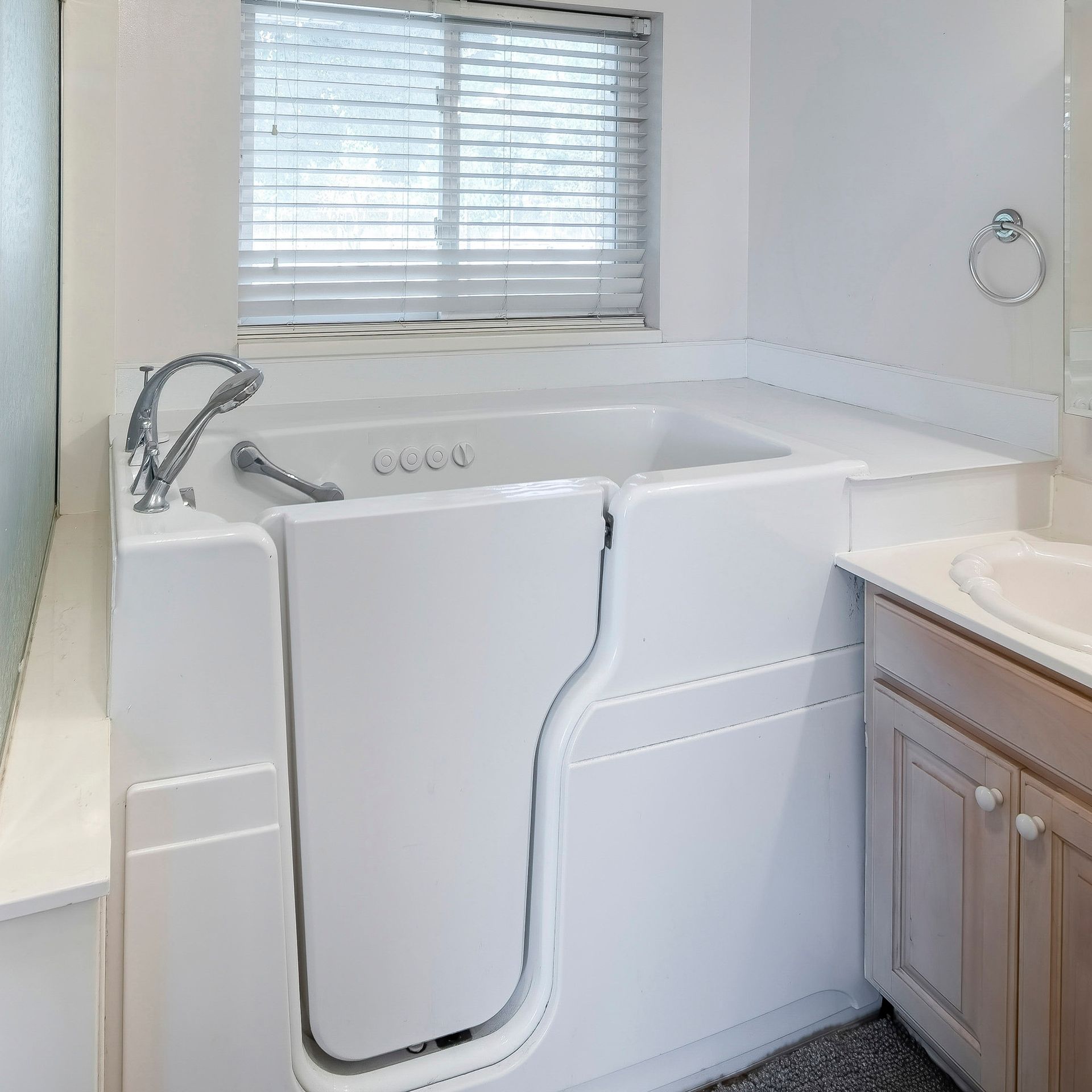 White walk-in bathtub with a door in a bathroom with a window, and a vanity with a sink.
