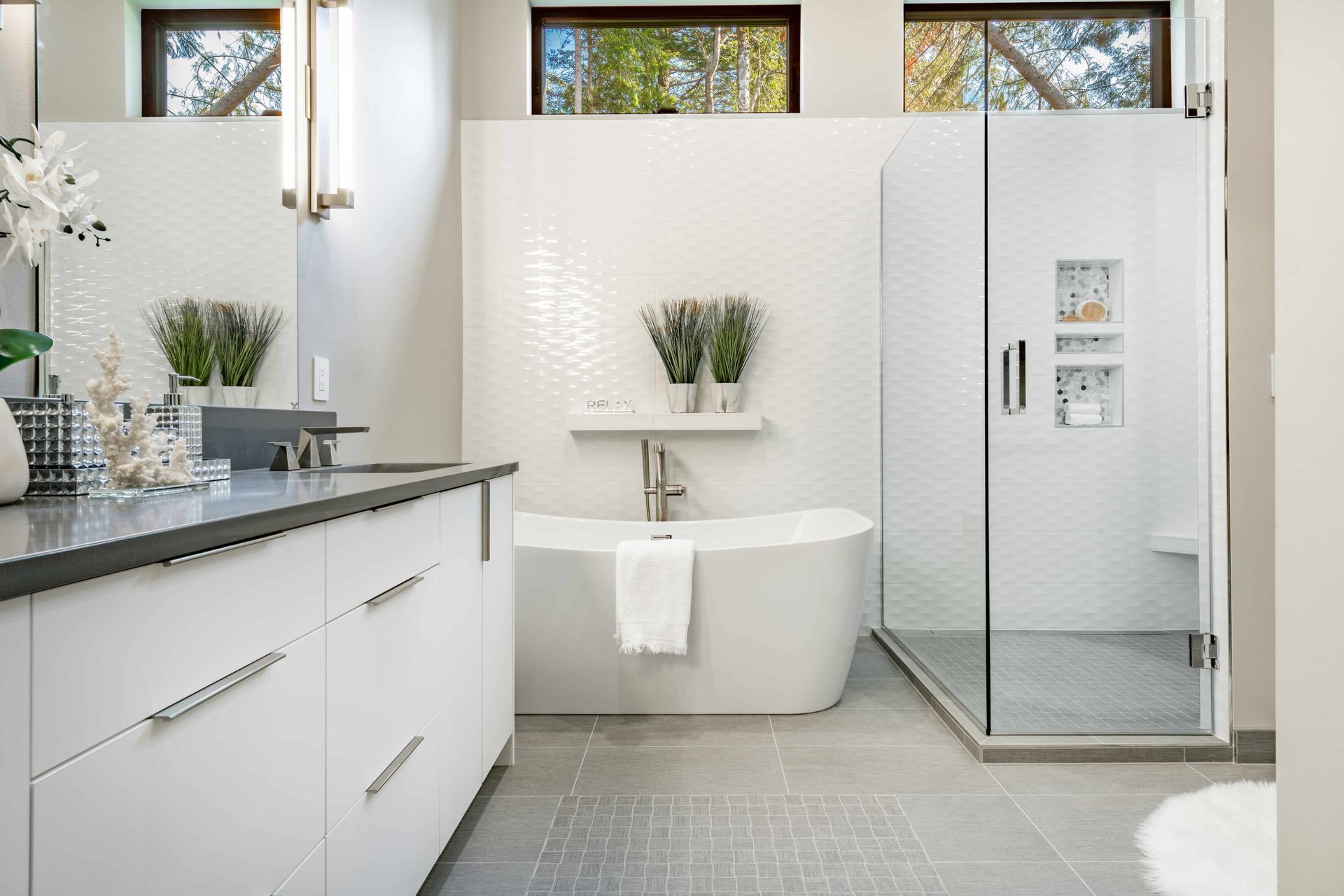 Modern white bathroom with a tub, shower, and vanity; gray tile floors; windows.
