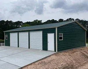 a green garage with three white garage doors and a window