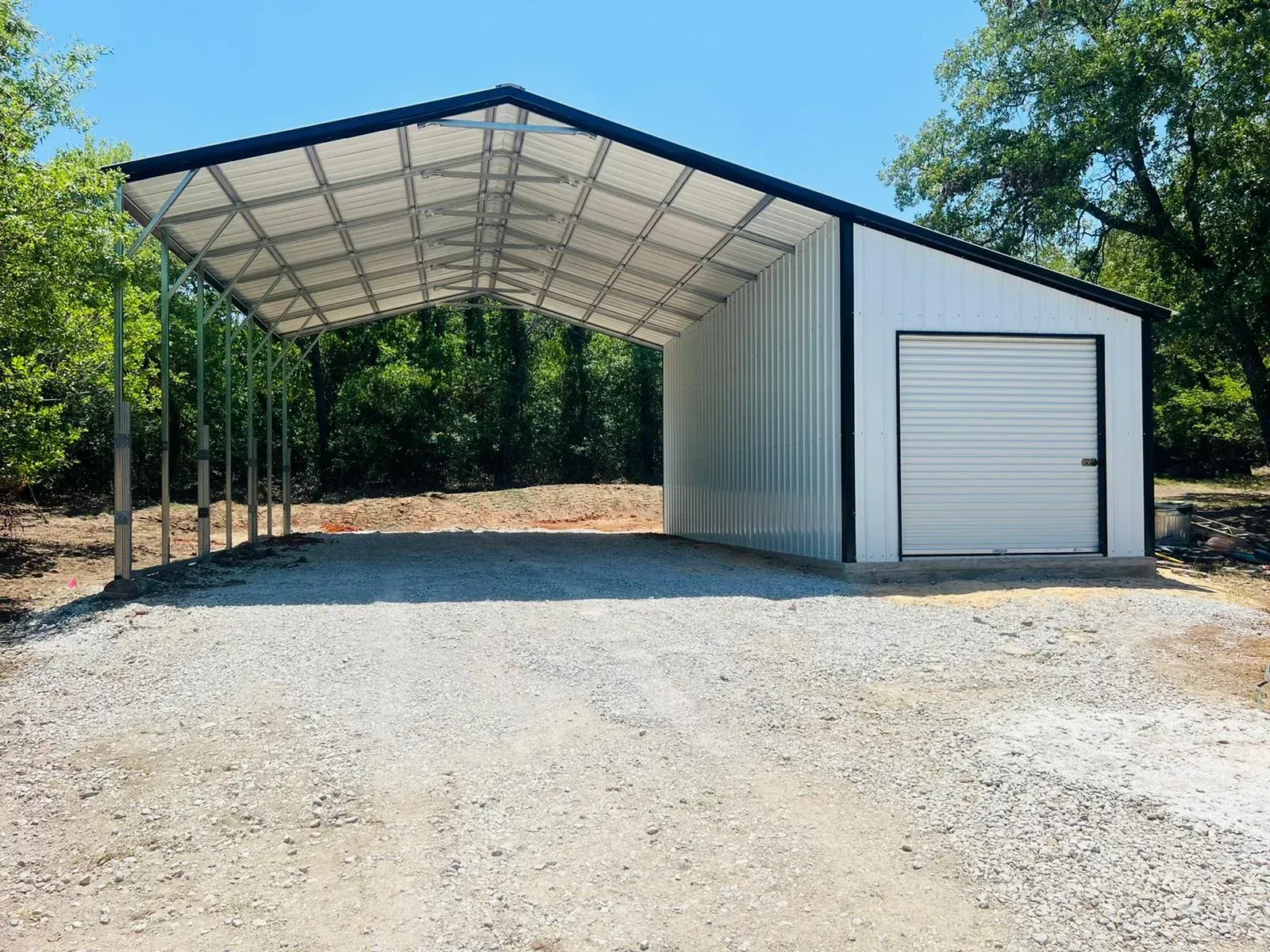 a white garage with a black roof is sitting on top of a gravel road