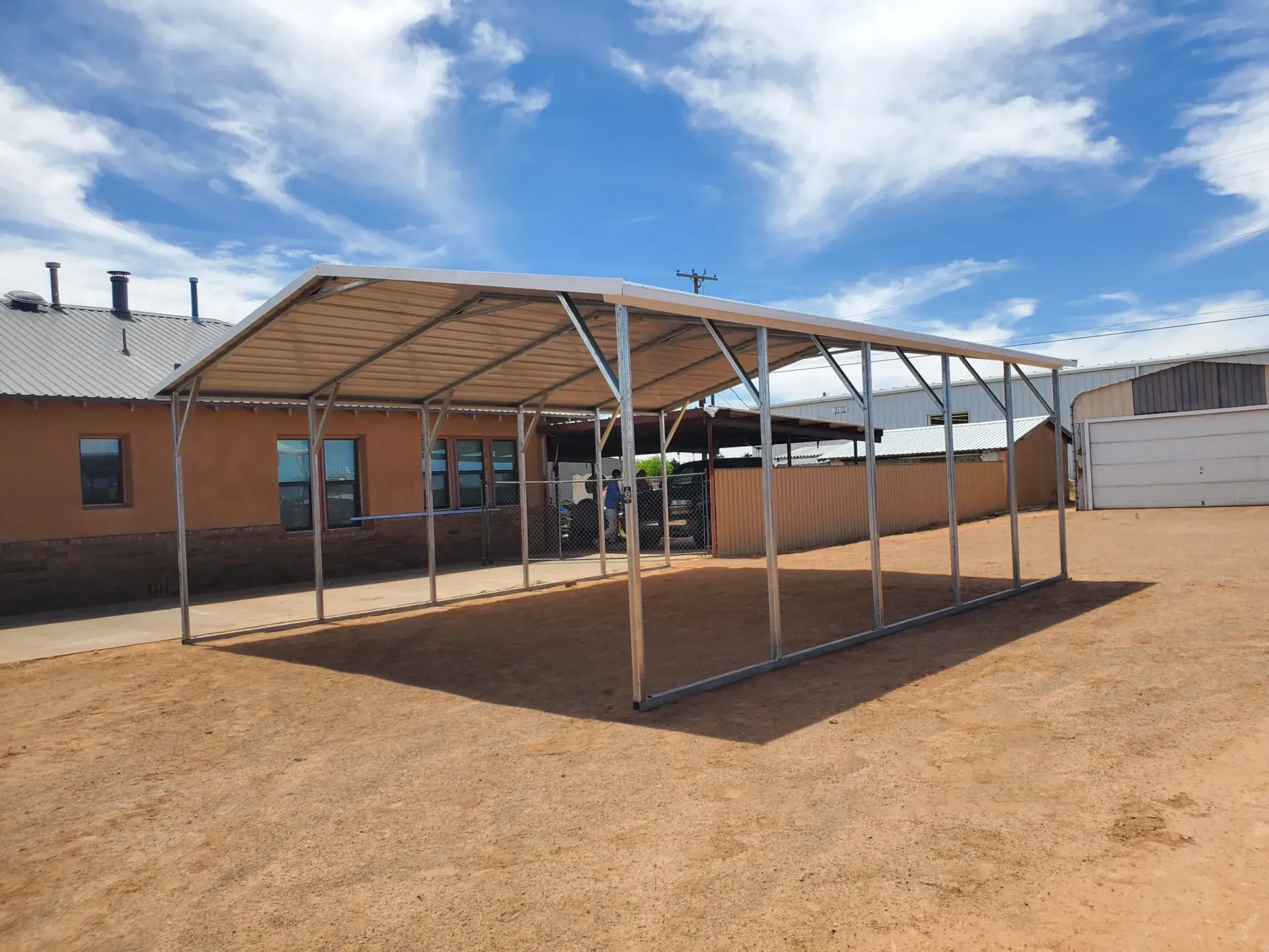 a metal carport is sitting in the dirt in front of a building