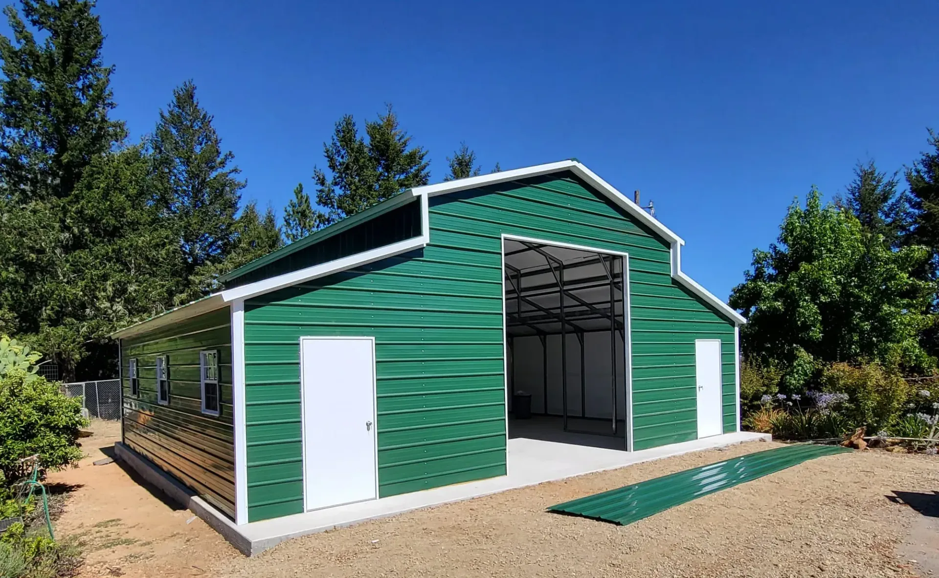 a green barn with a white roof is sitting on top of a dirt field