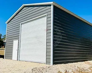 a black garage with a white door is sitting on top of a gravel lot