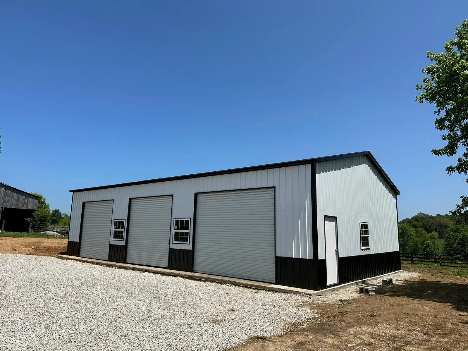a white and black garage with two garage doors is sitting on top of a gravel lot