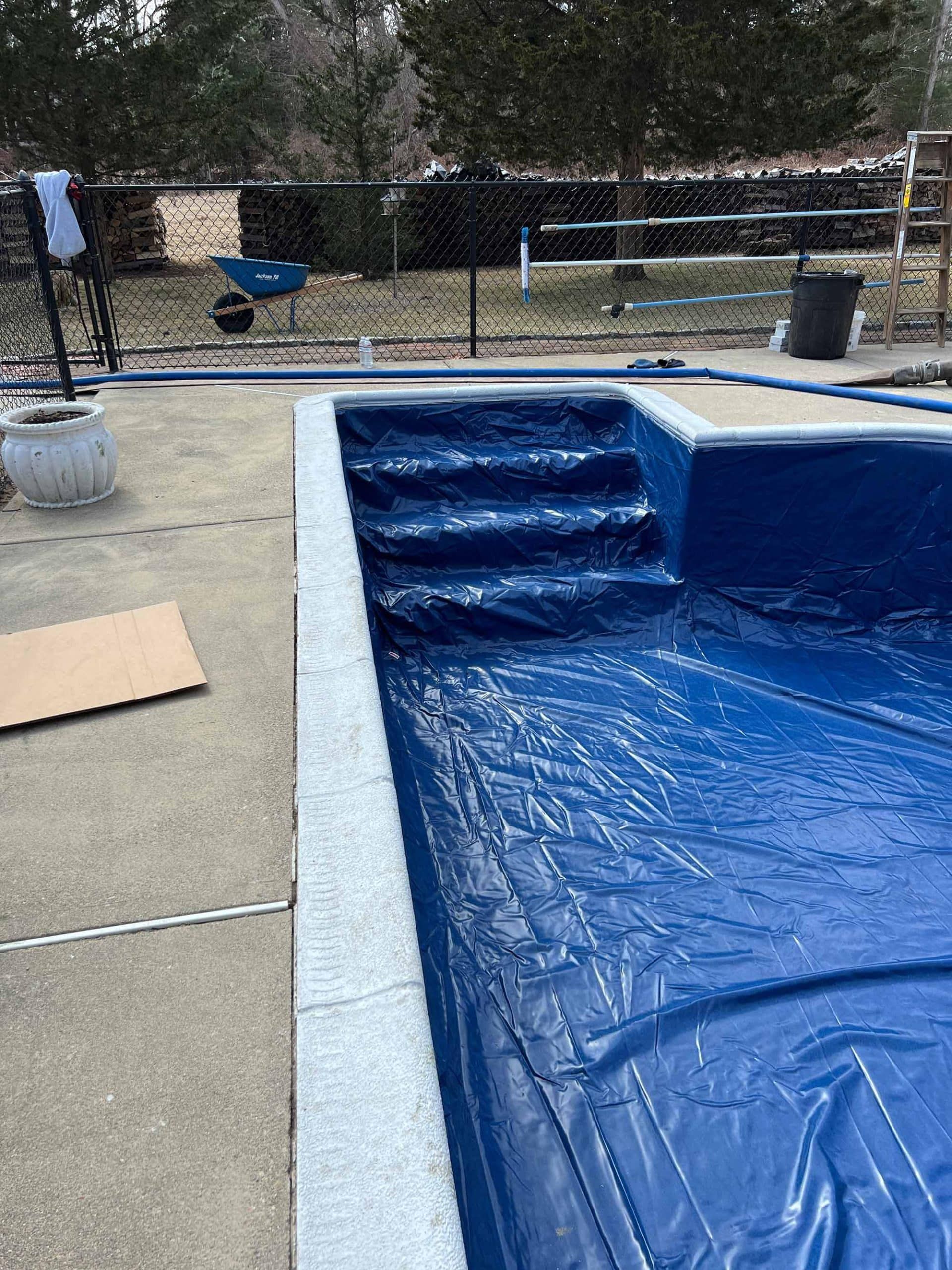 A swimming pool covered with a blue plastic tarp, featuring built-in stairs on a concrete patio.