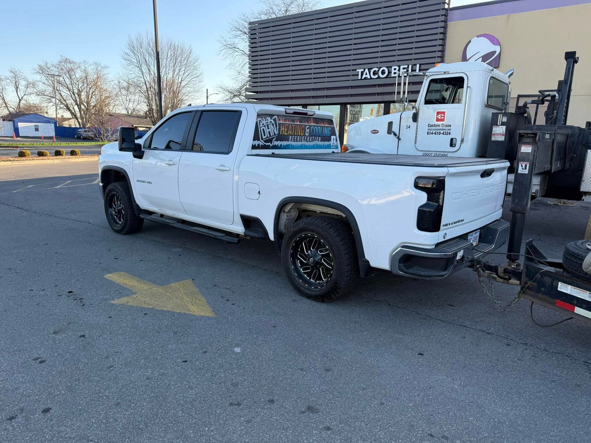 White pickup truck parked outside a Taco Bell. Truck has black wheels and a trailer hitched to the back.