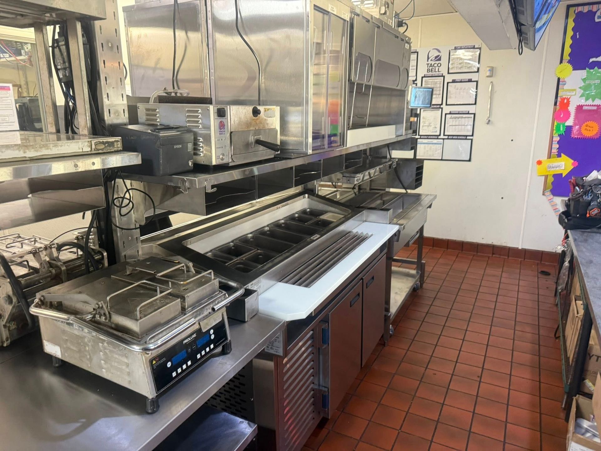 Commercial kitchen with stainless steel appliances and red tile floor.