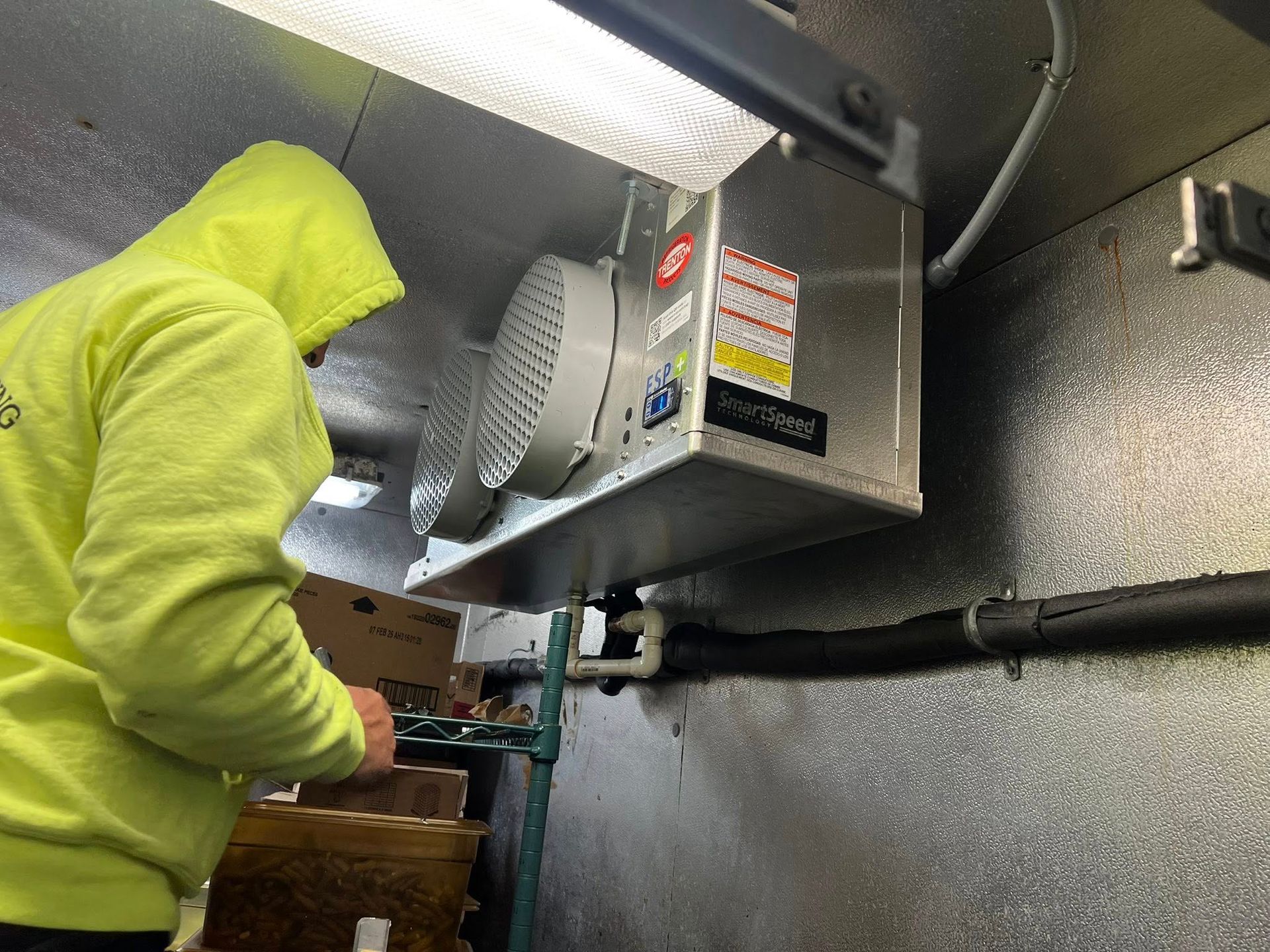 Person in yellow hoodie working in a cold storage unit with refrigeration equipment.