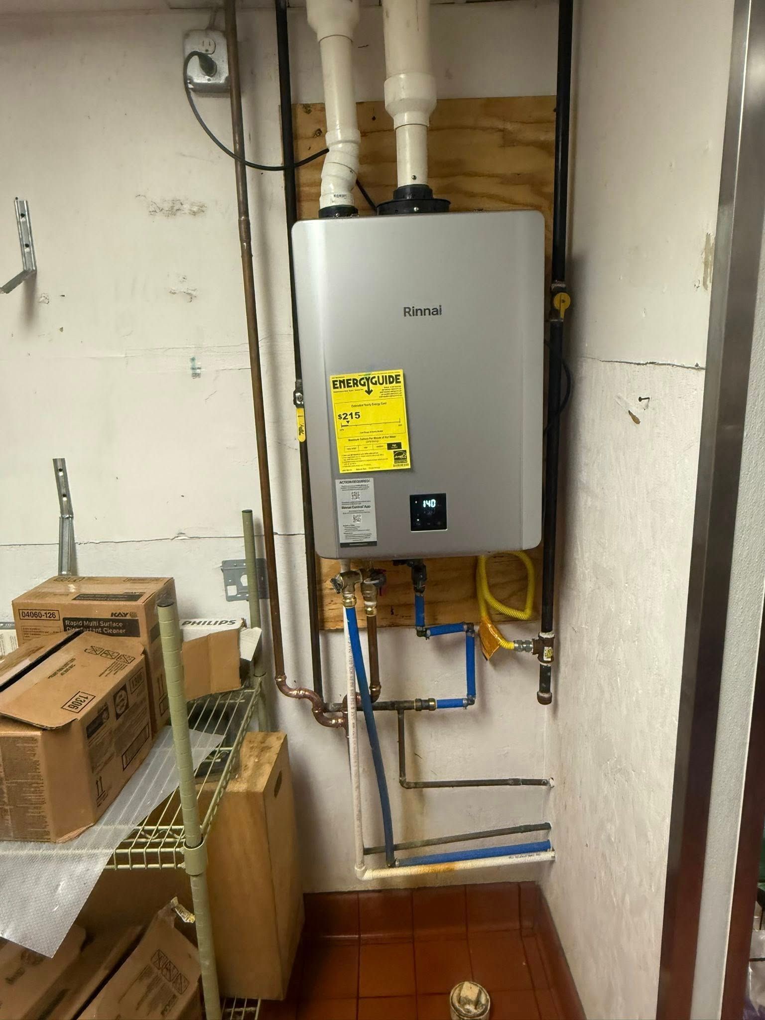 Tankless water heater installed on a wall with pipes and gas lines in a commercial space.