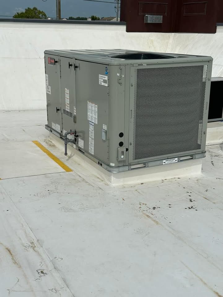 HVAC unit on a white rooftop. Gray metal box with a large grid, on a raised white base. Yellow line nearby.