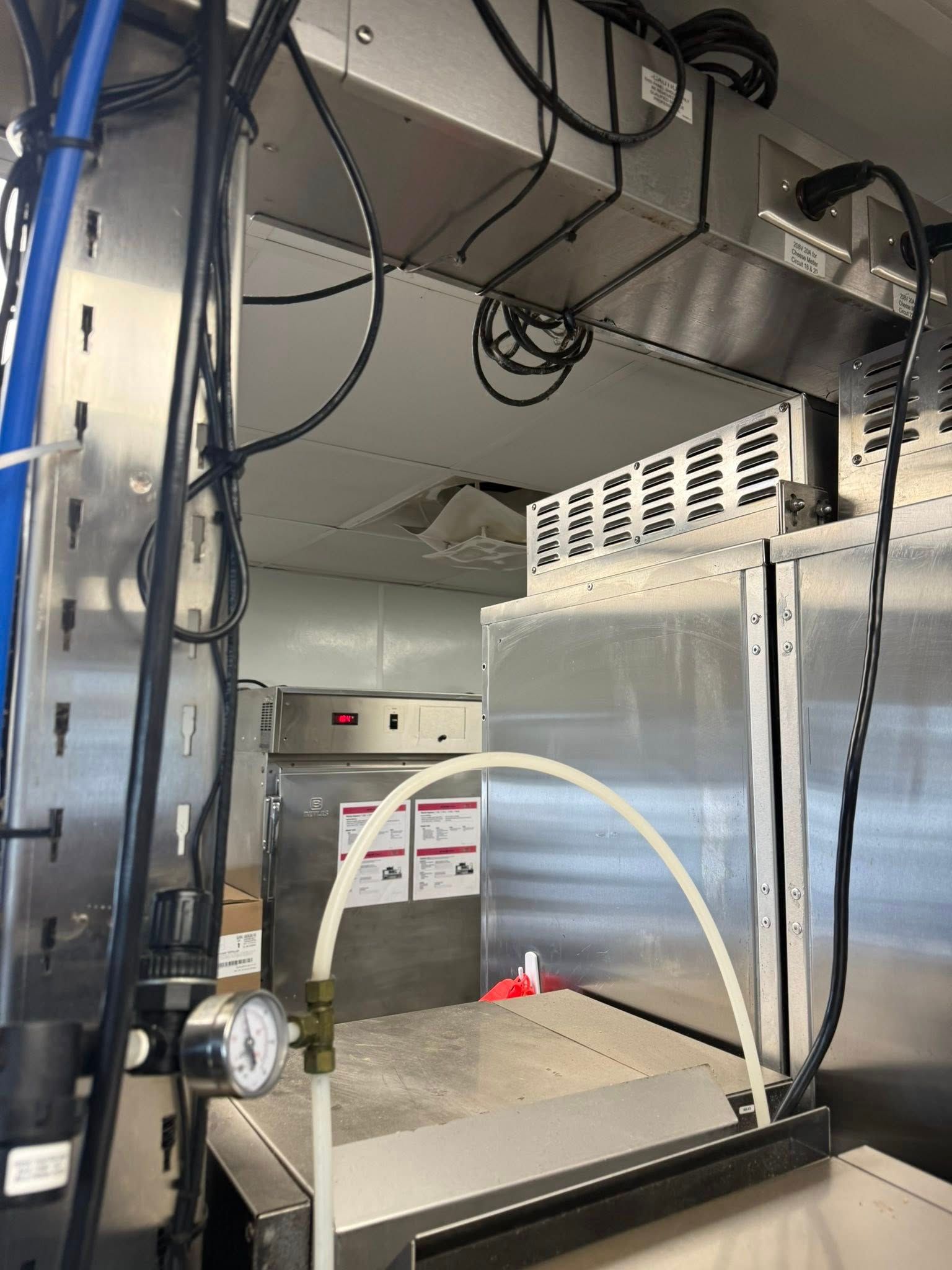 Interior of a commercial kitchen with stainless steel appliances, ventilation, and a water line.